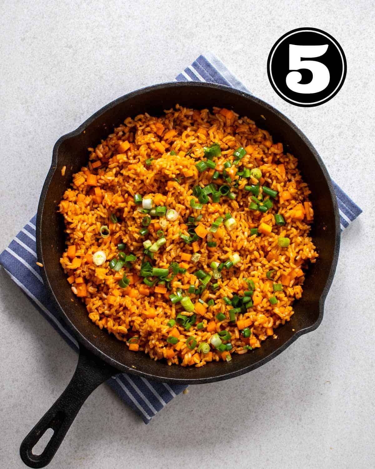 Adding chopped green onion to a pan of gochujang fried rice on a blue folded teacloth.