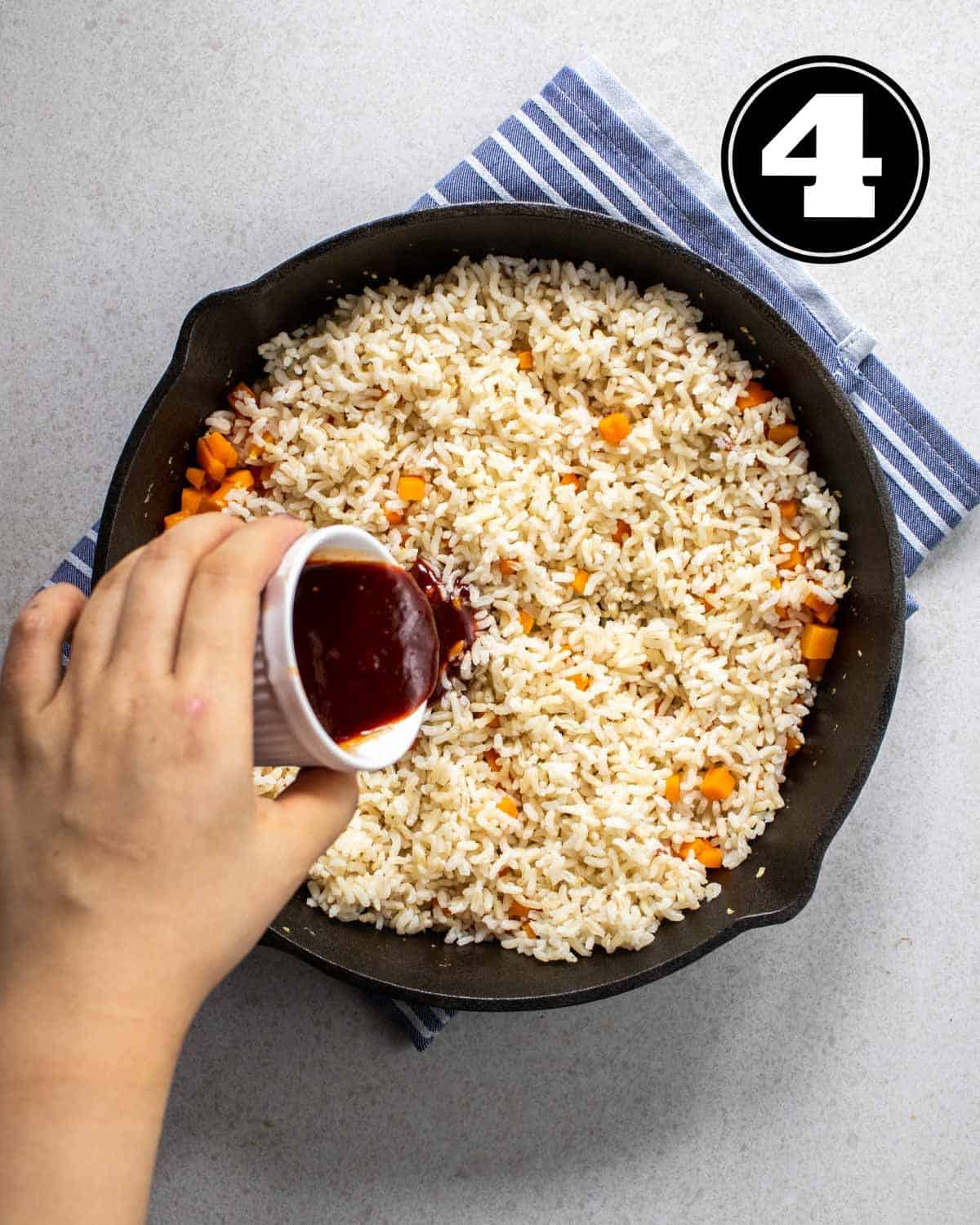 Pouring gochujang sauce into a pan of rice and carrot cubes.