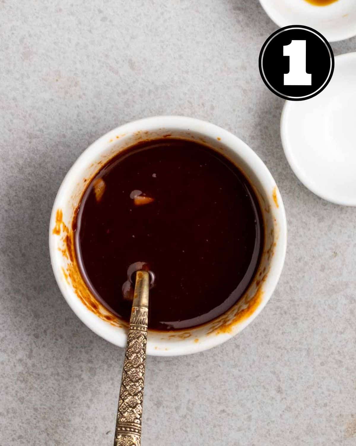 Gochujang sauce in a ramekin with a spoon and 2 sauce dishes in the background.