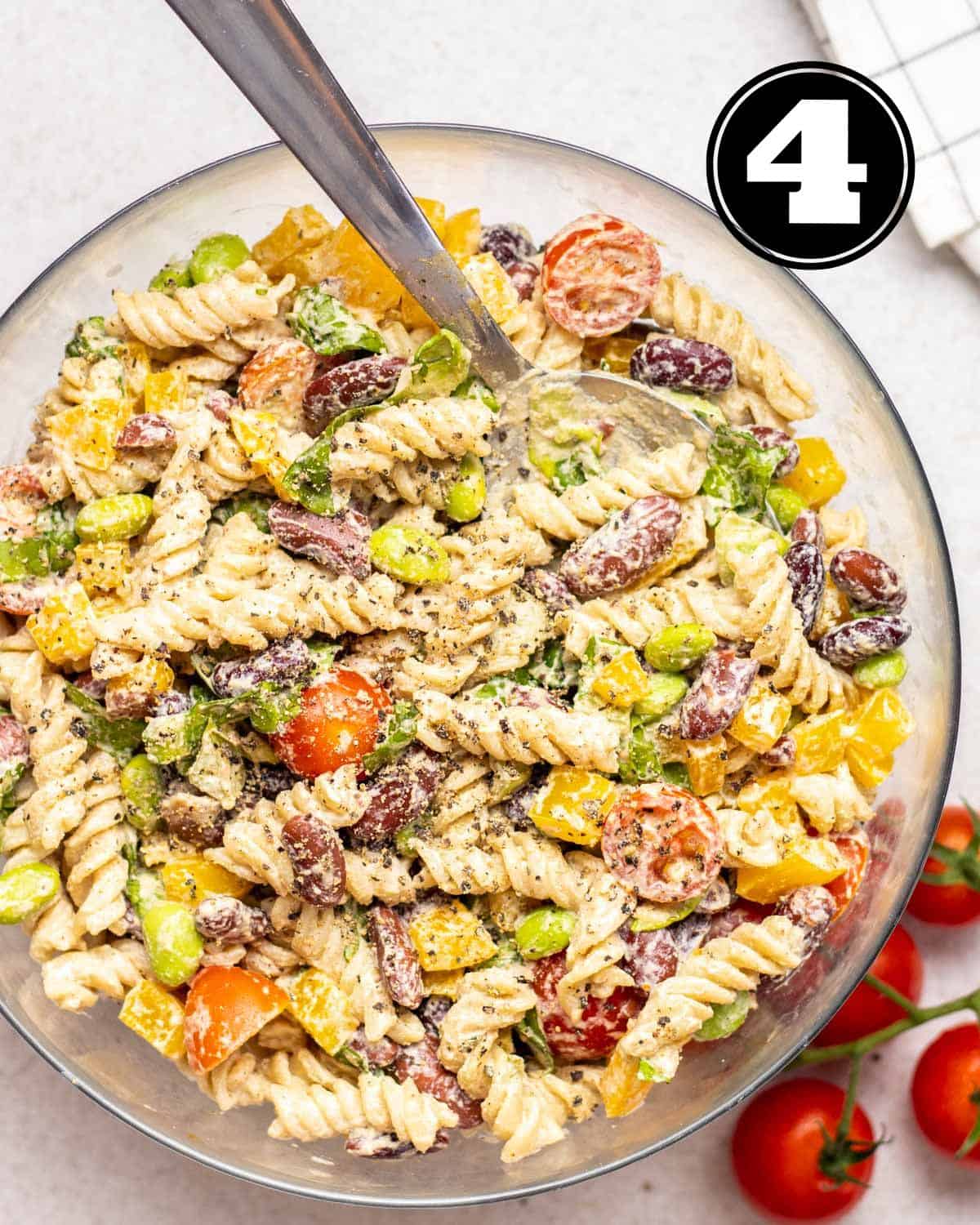 Protein pasta salad in a glass bowl with a serving spoon beside.