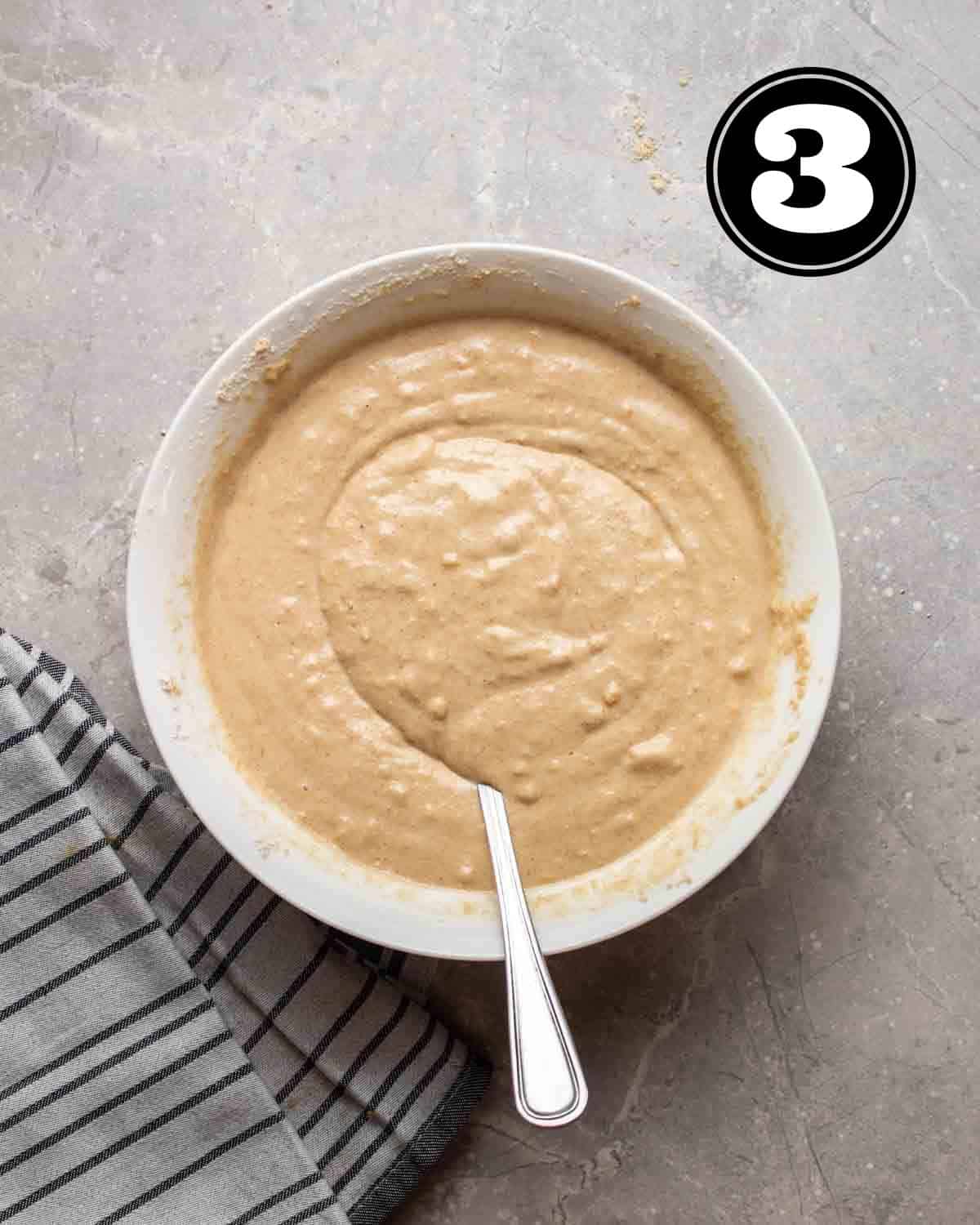 Waffle batter in a bowl with a spoon beside.