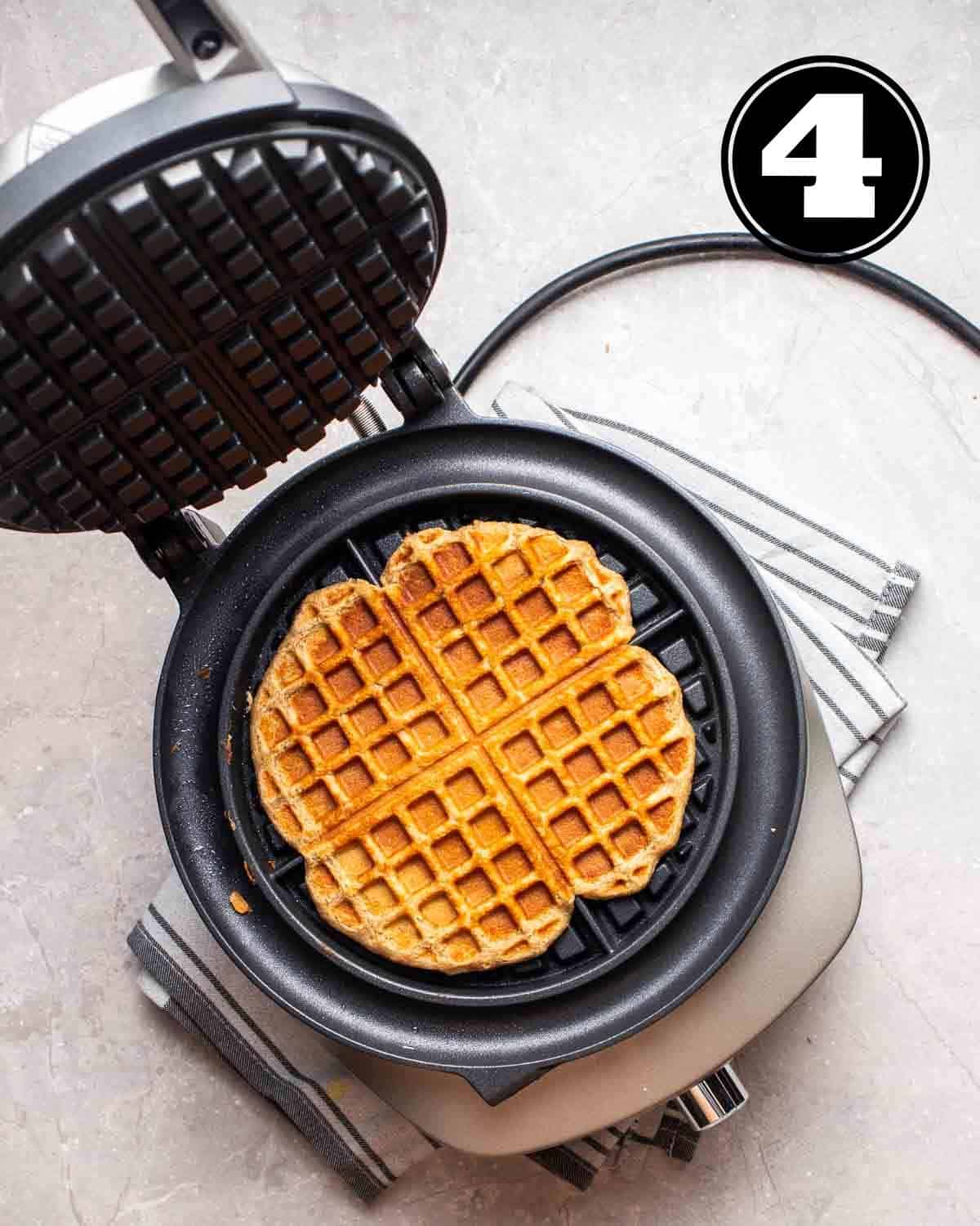 A cooked waffle in a waffle maker on a folded blue teacloth.