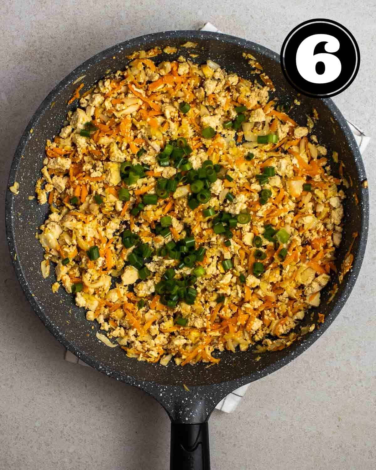 Adding green onion into a pan of tofu and vegetable filling on a white folded teacloth.
