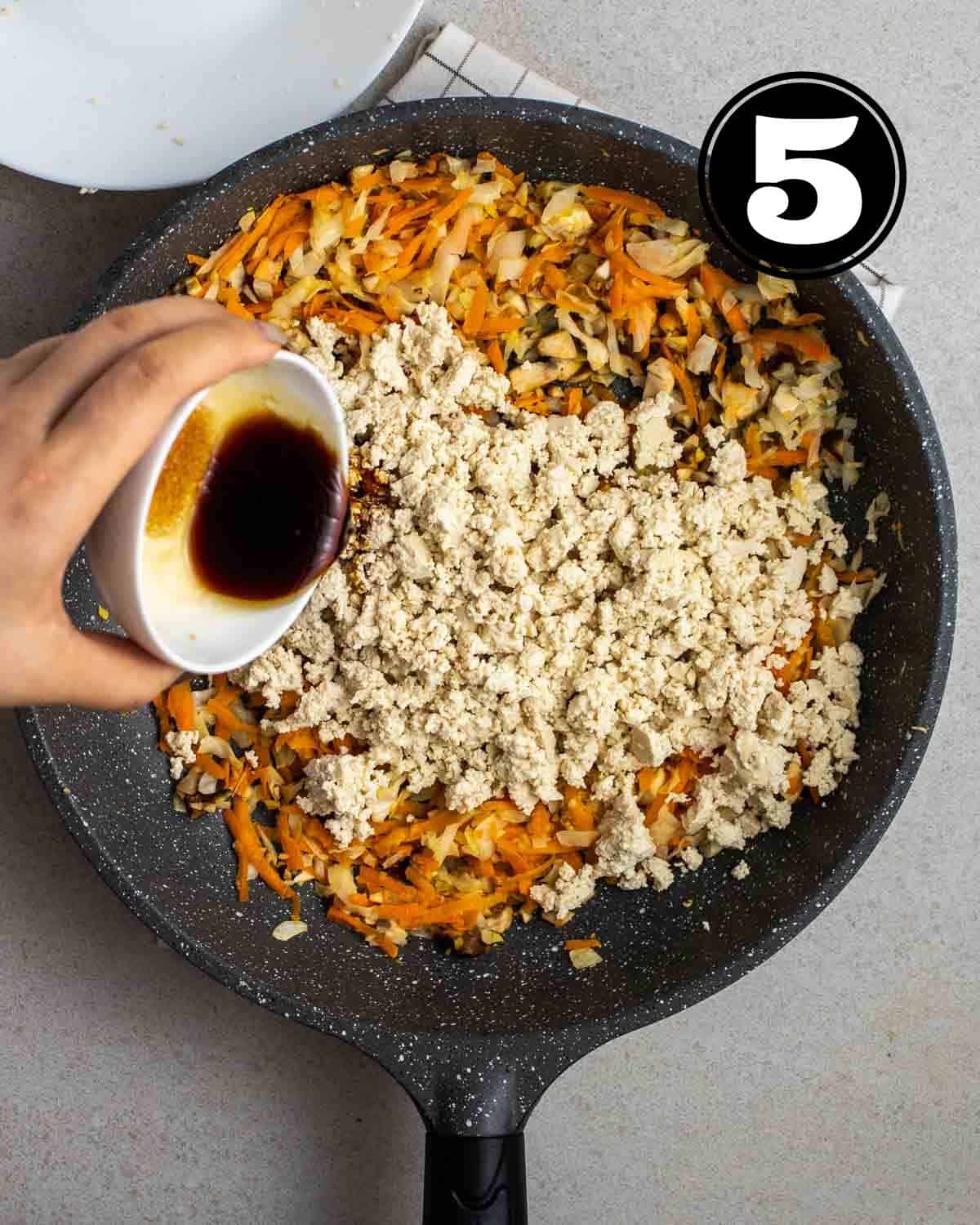 Pouring sauce into a pan of cooked vegetables and crumbled tofu.