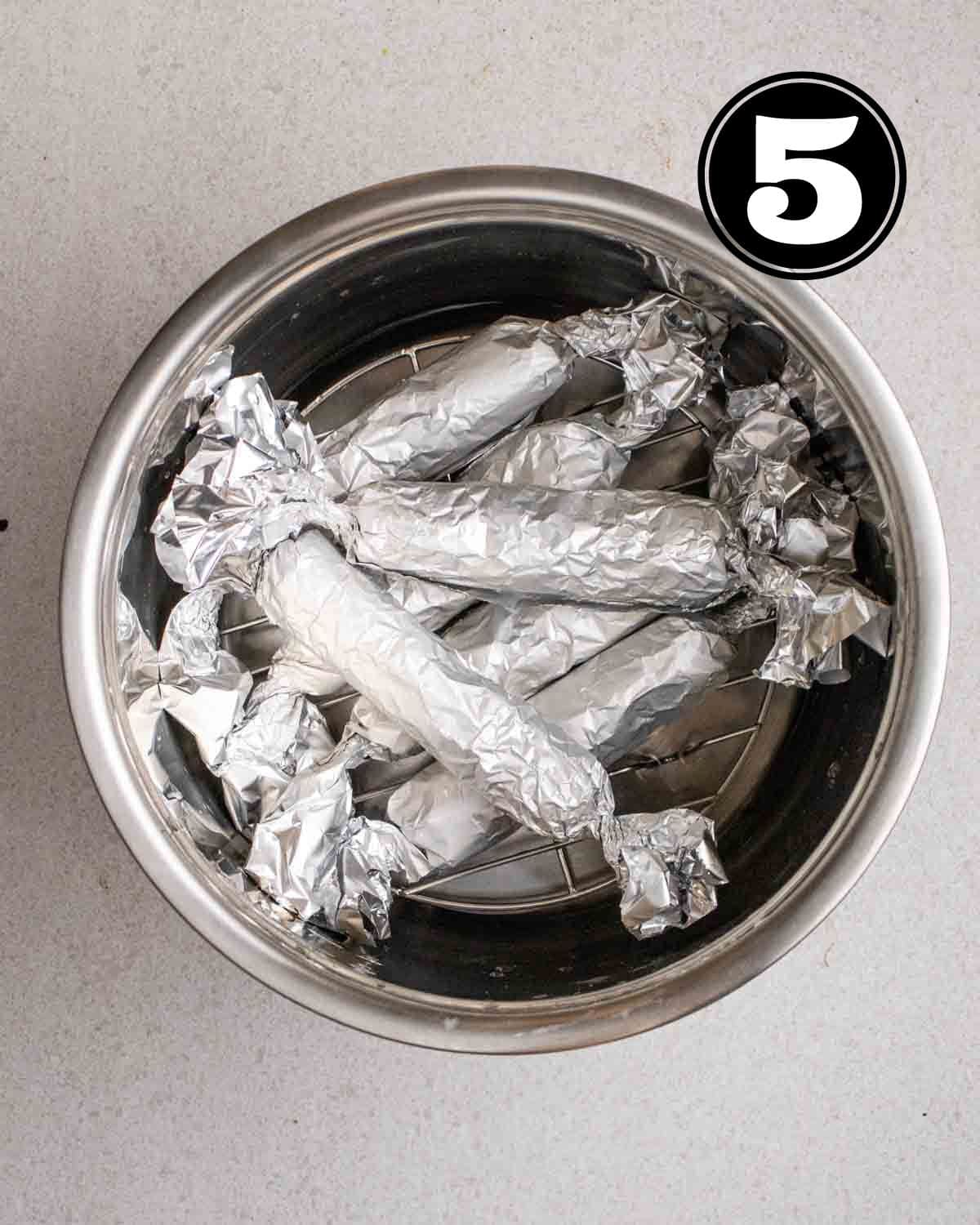 Shaped vegan sausages wrapped in foil in a pot.
