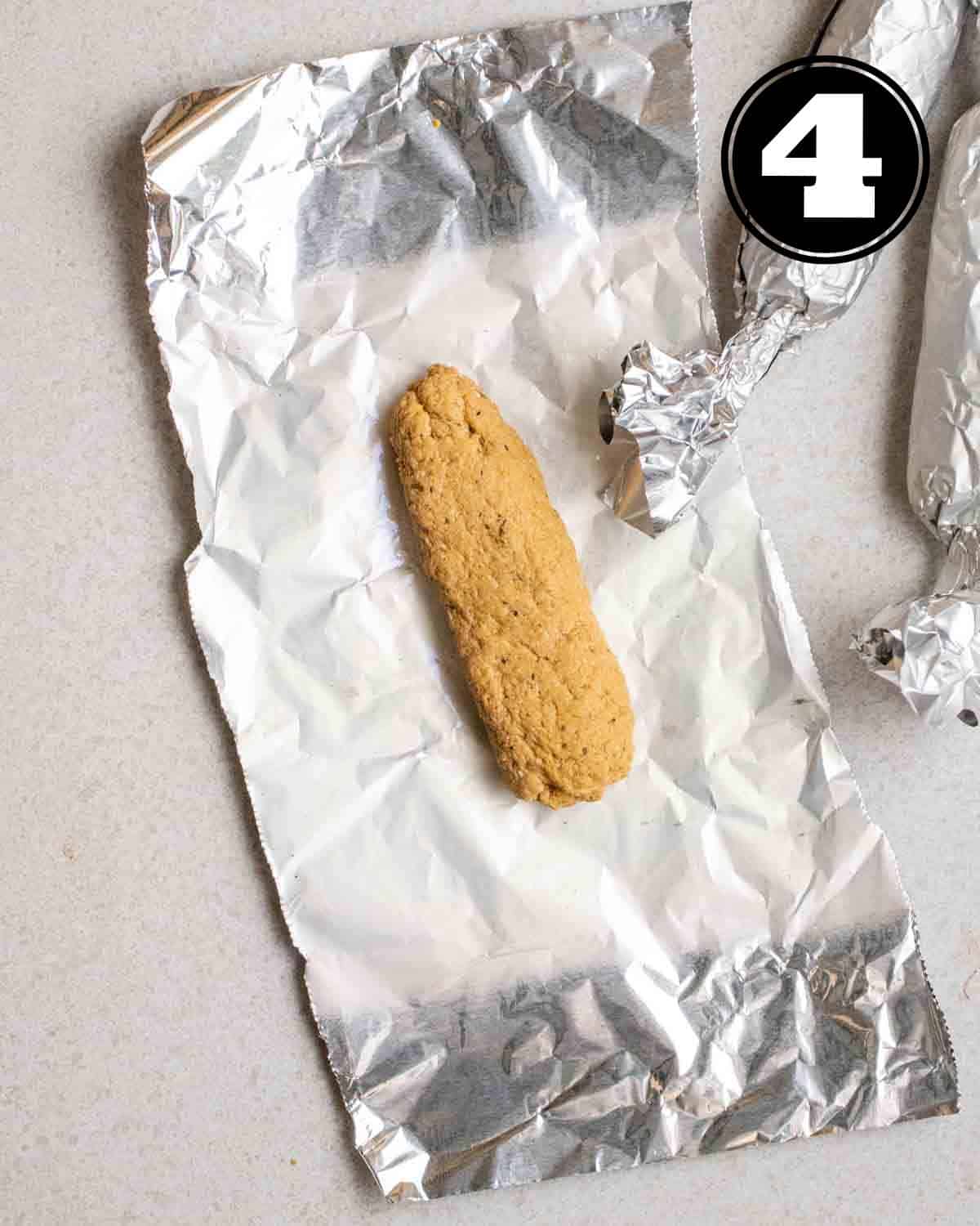 Seitan dough shaped into a log on an aluminum foil.