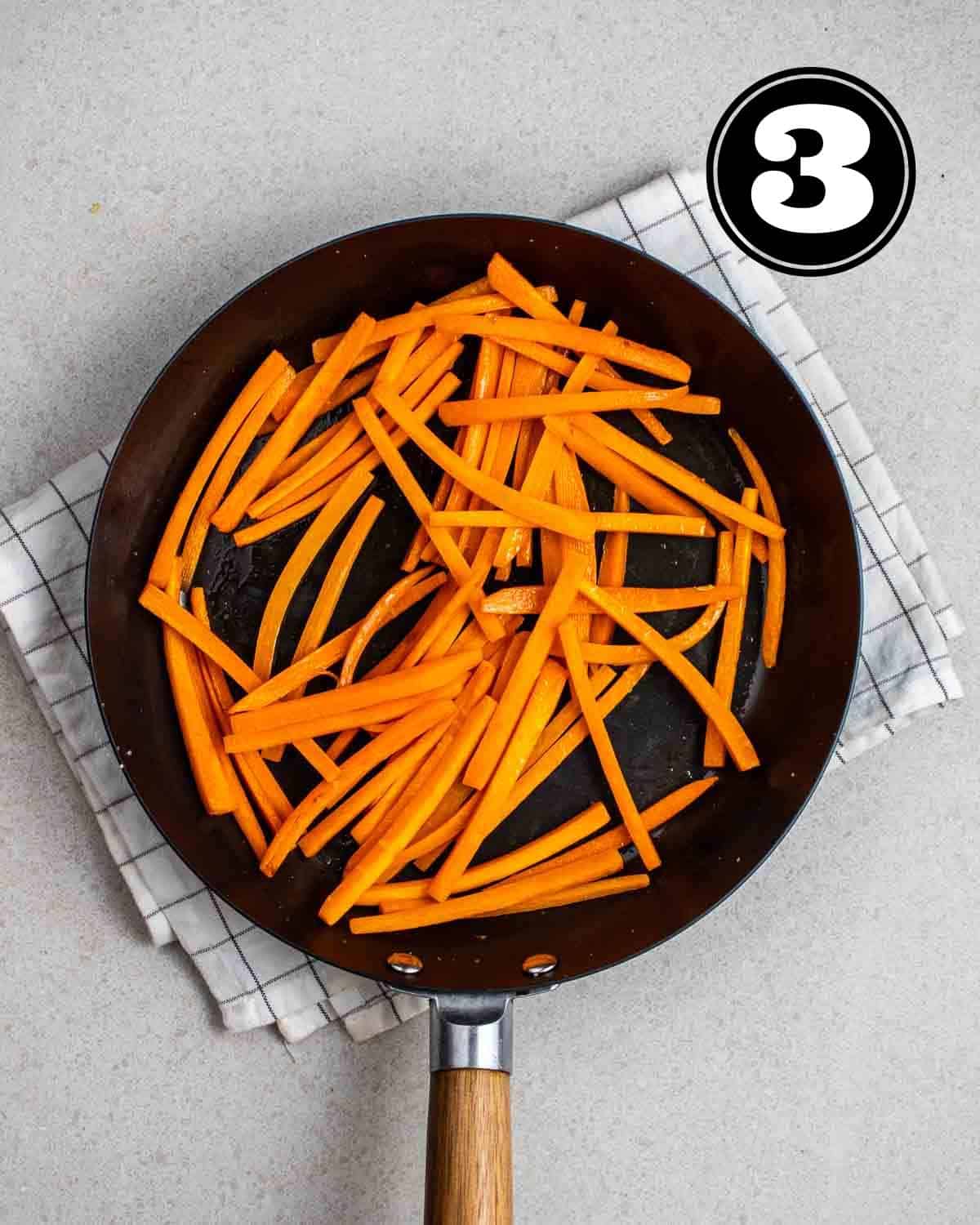 Sauteed carrot in a pan on a folded white teacloth.