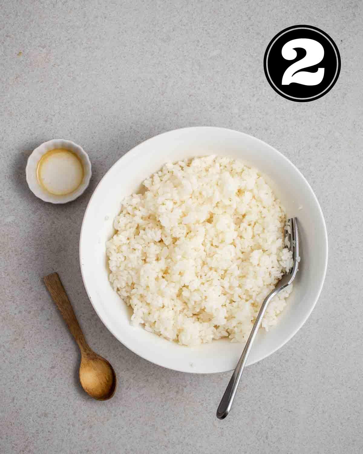 Seasoned rice in a bowl with a fork beside with a sauce dish and wooden spoon in the background.