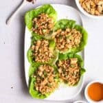 A plate of tofu lettuce wrap with tea, bowl of tofu filling, and spoonful of chili flakes beside.