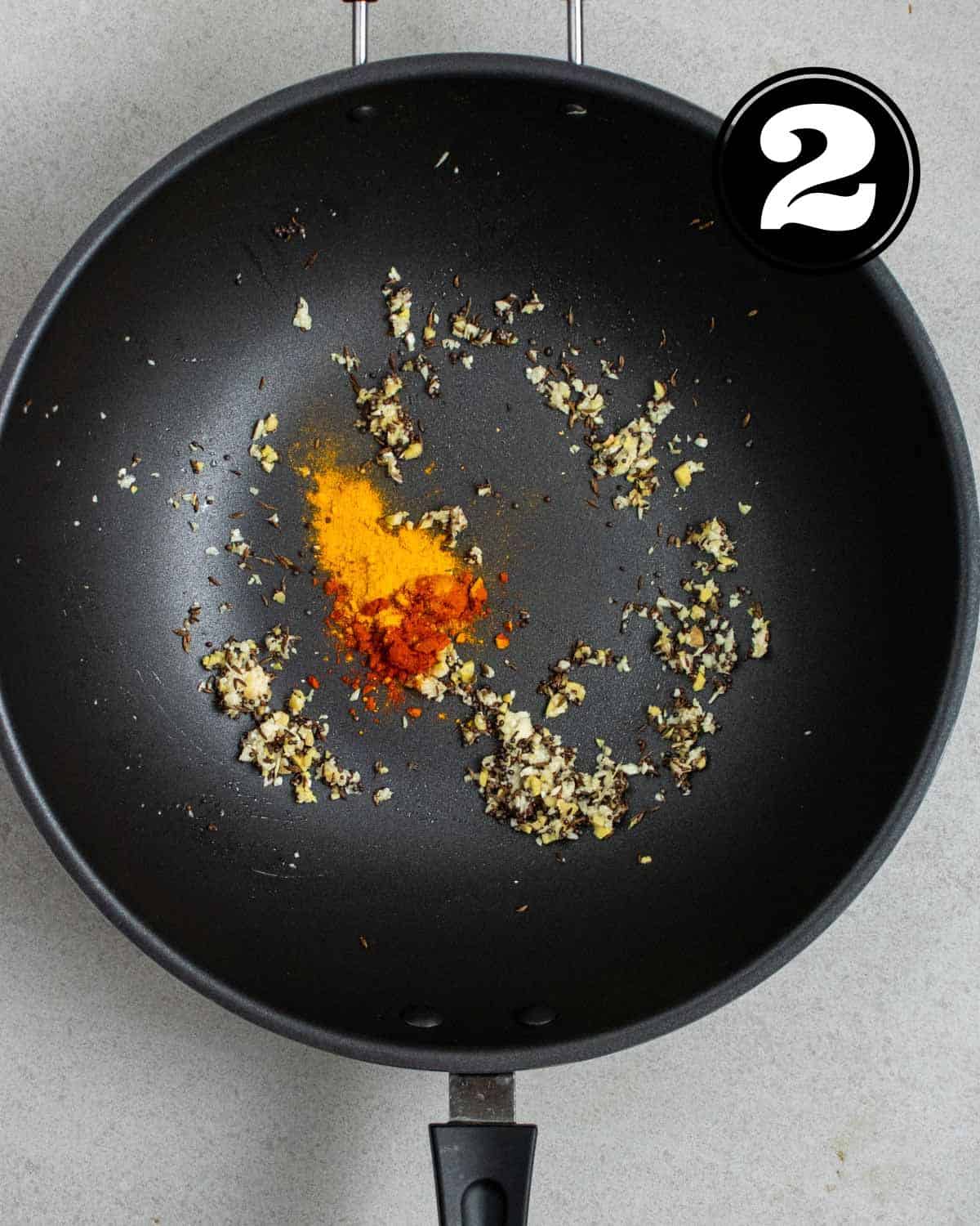 Ground spices, cooked garlic, cumin and mustard seeds in a wok.