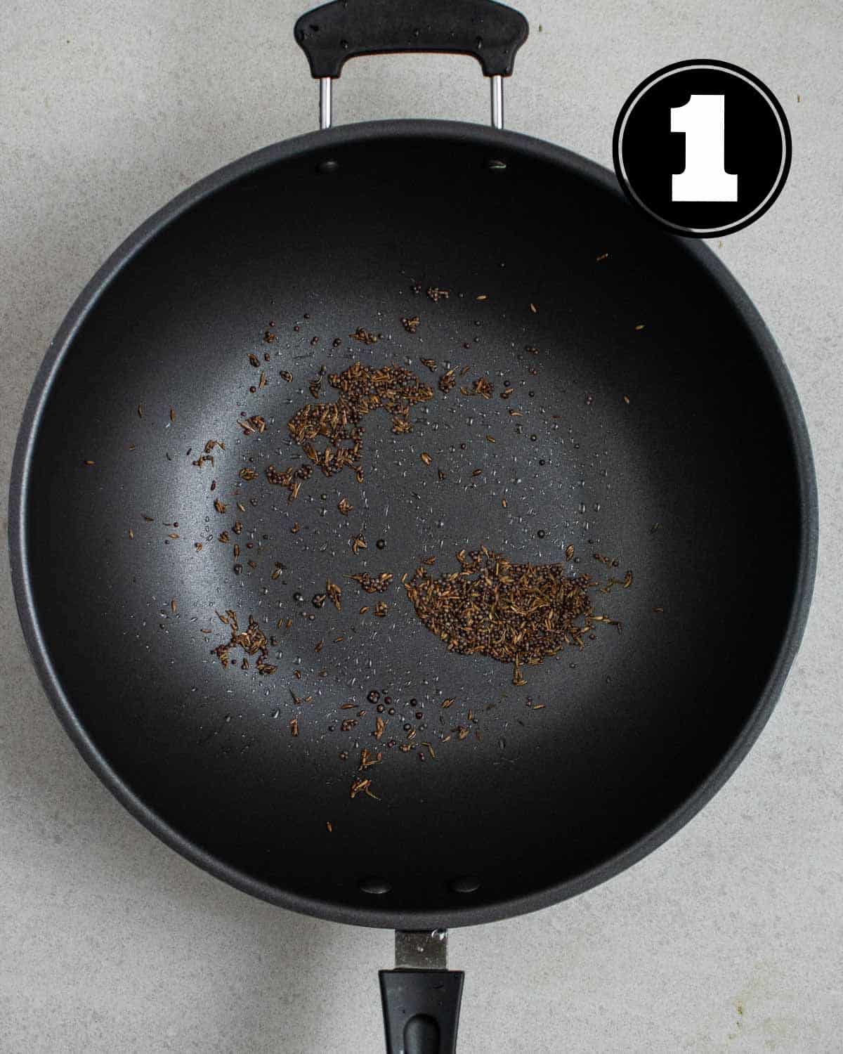Cumin and mustard seeds in a wok.