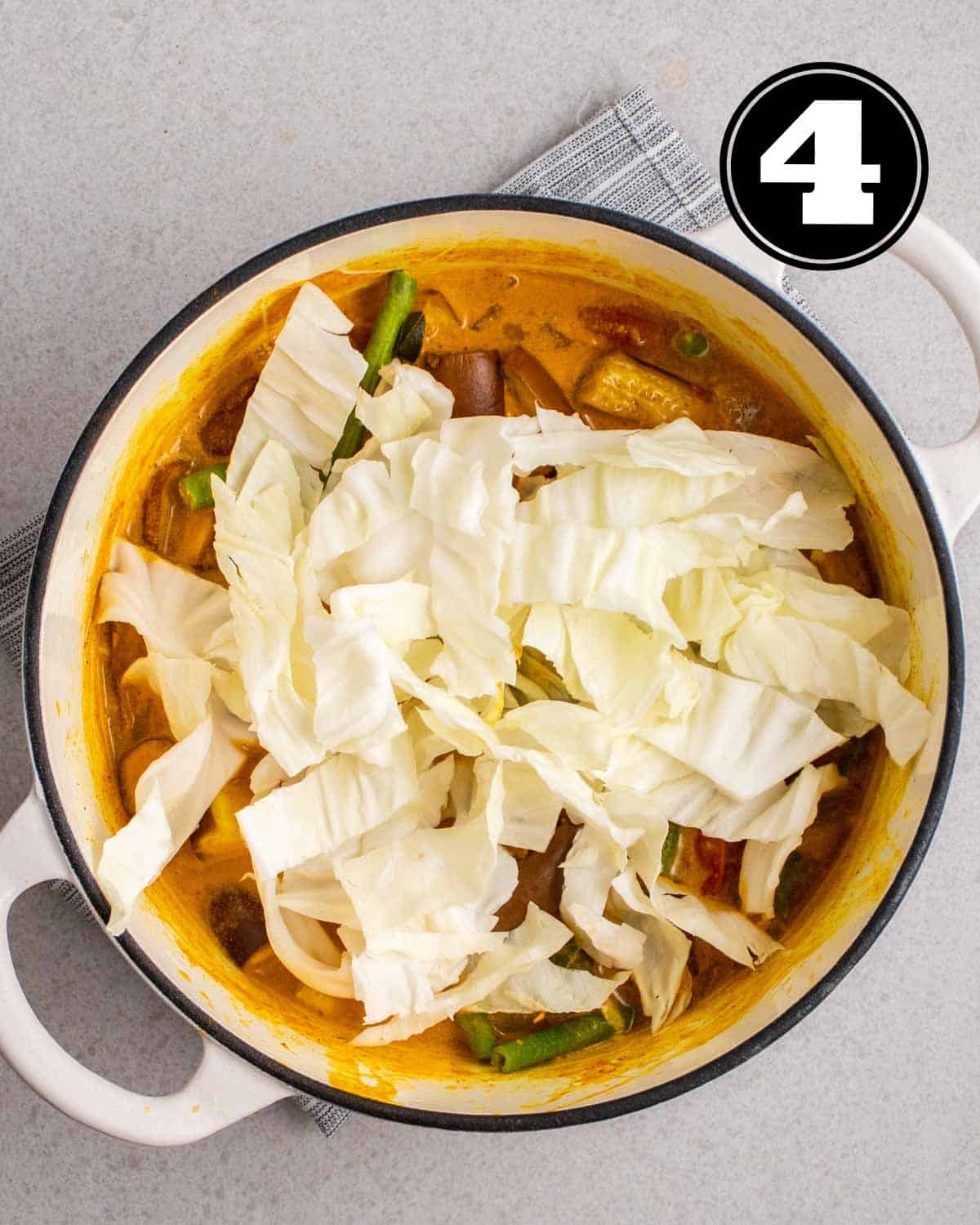 Adding sliced cabbage into a pot of vegetable curry in a white Dutch oven.