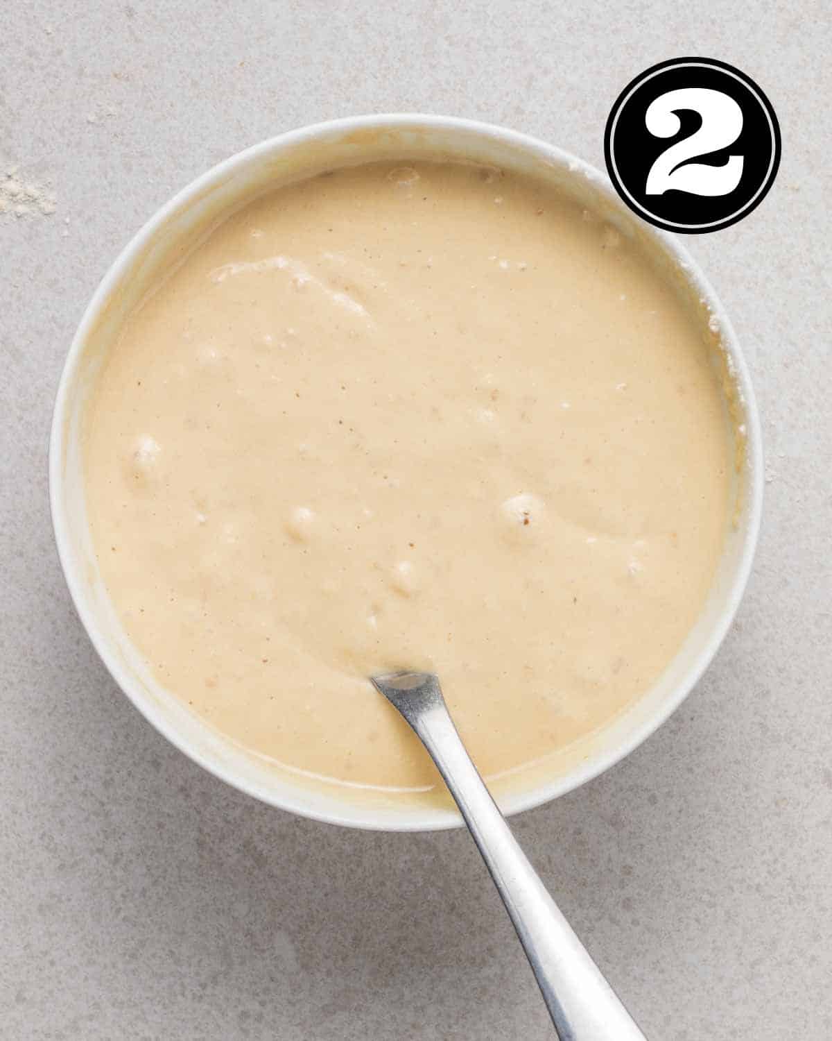 Pancake batter in a bowl with a spoon beside.