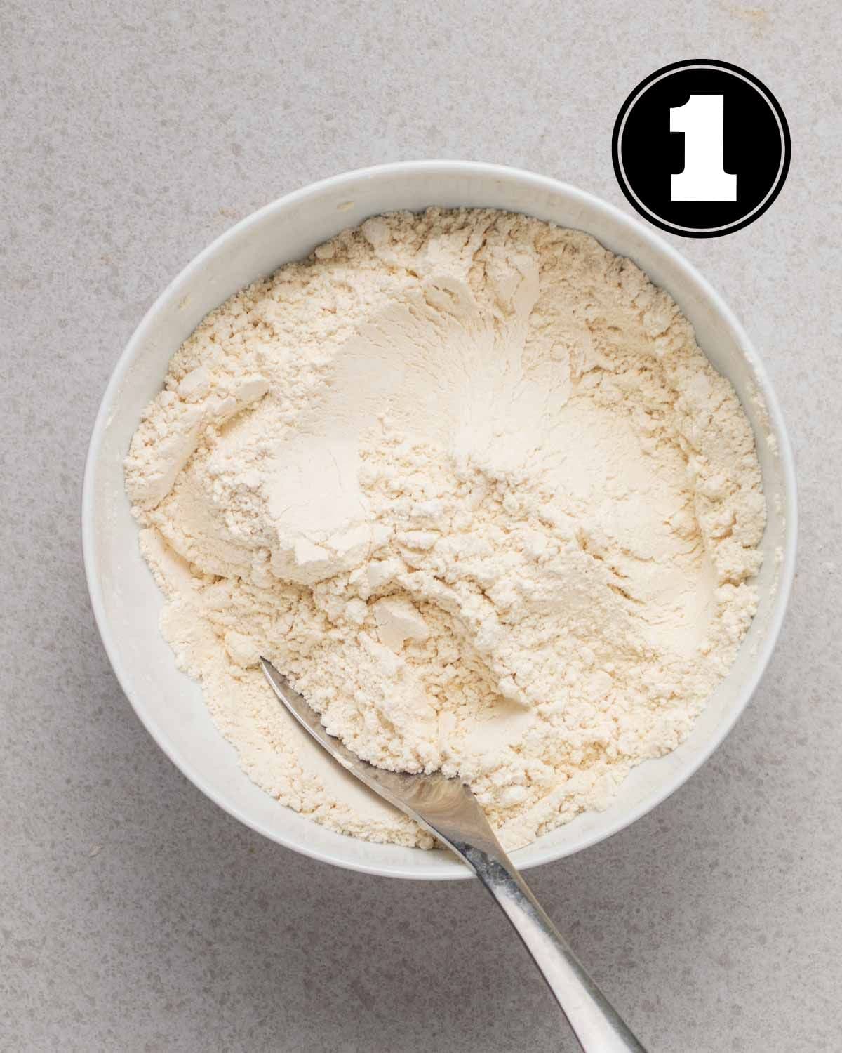Dry ingredients in a bowl with a spoon beside.