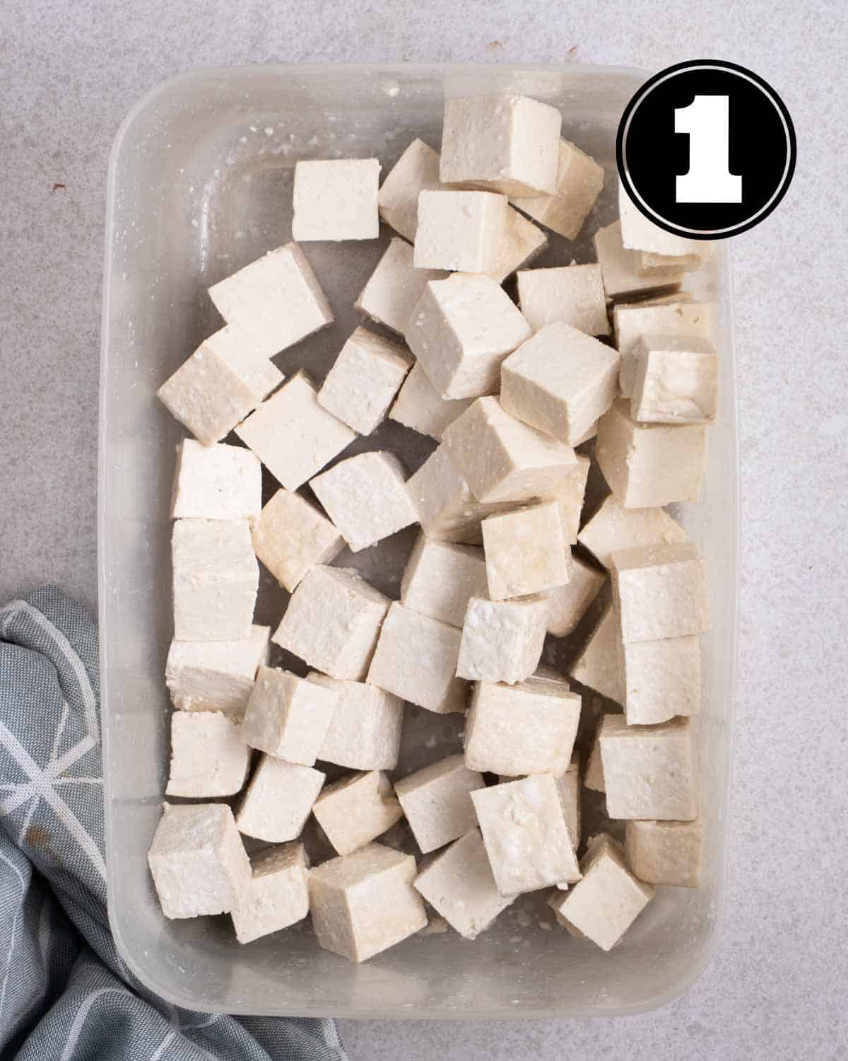 Coated tofu in a container with a blue teacloth beside.