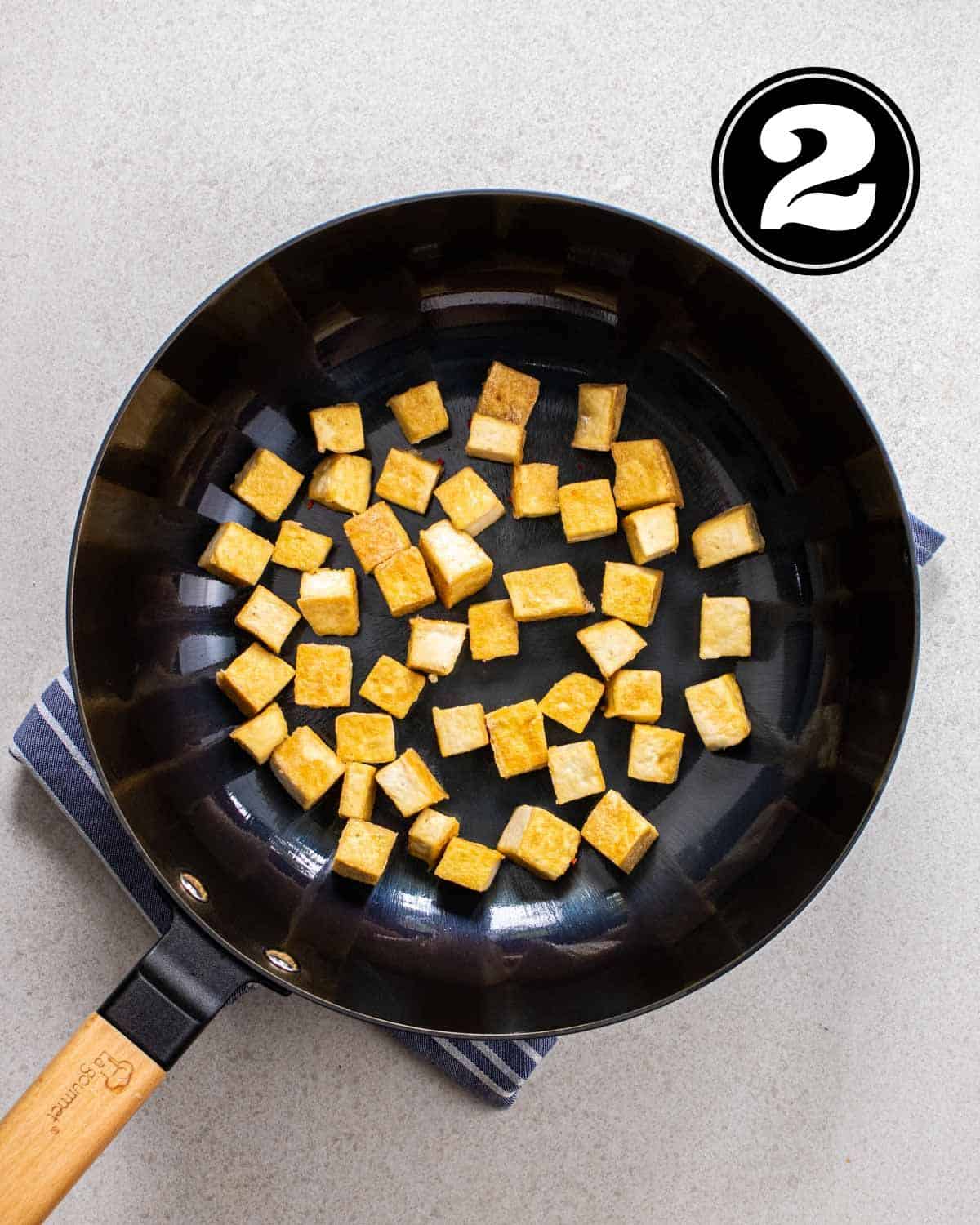 Pan-fried tofu in a wok on a folded white and blue teacloth.