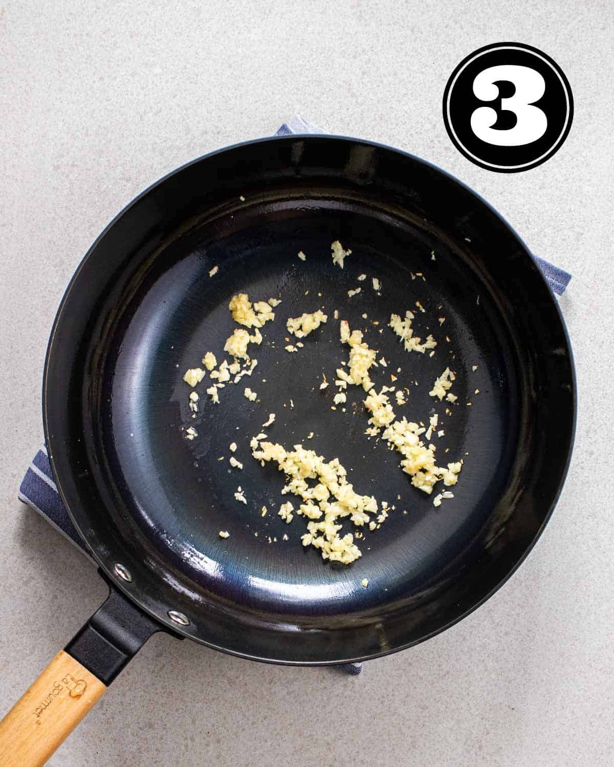 Fried garlic in a cast iron wok on a blue and white folded teacloth.