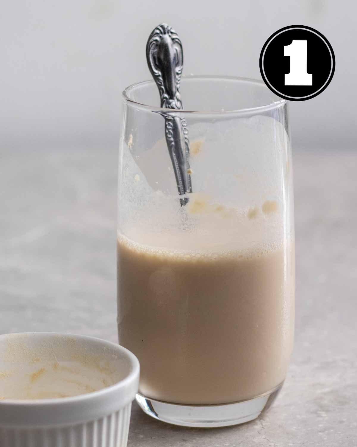 A glass of protein shake with a teaspoon and an empty ramekin beside.