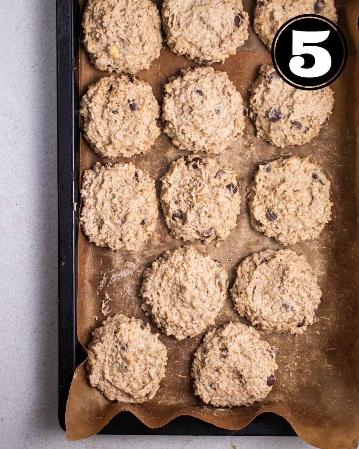 Unbaked cookies in a black baking tray lined with parchment.