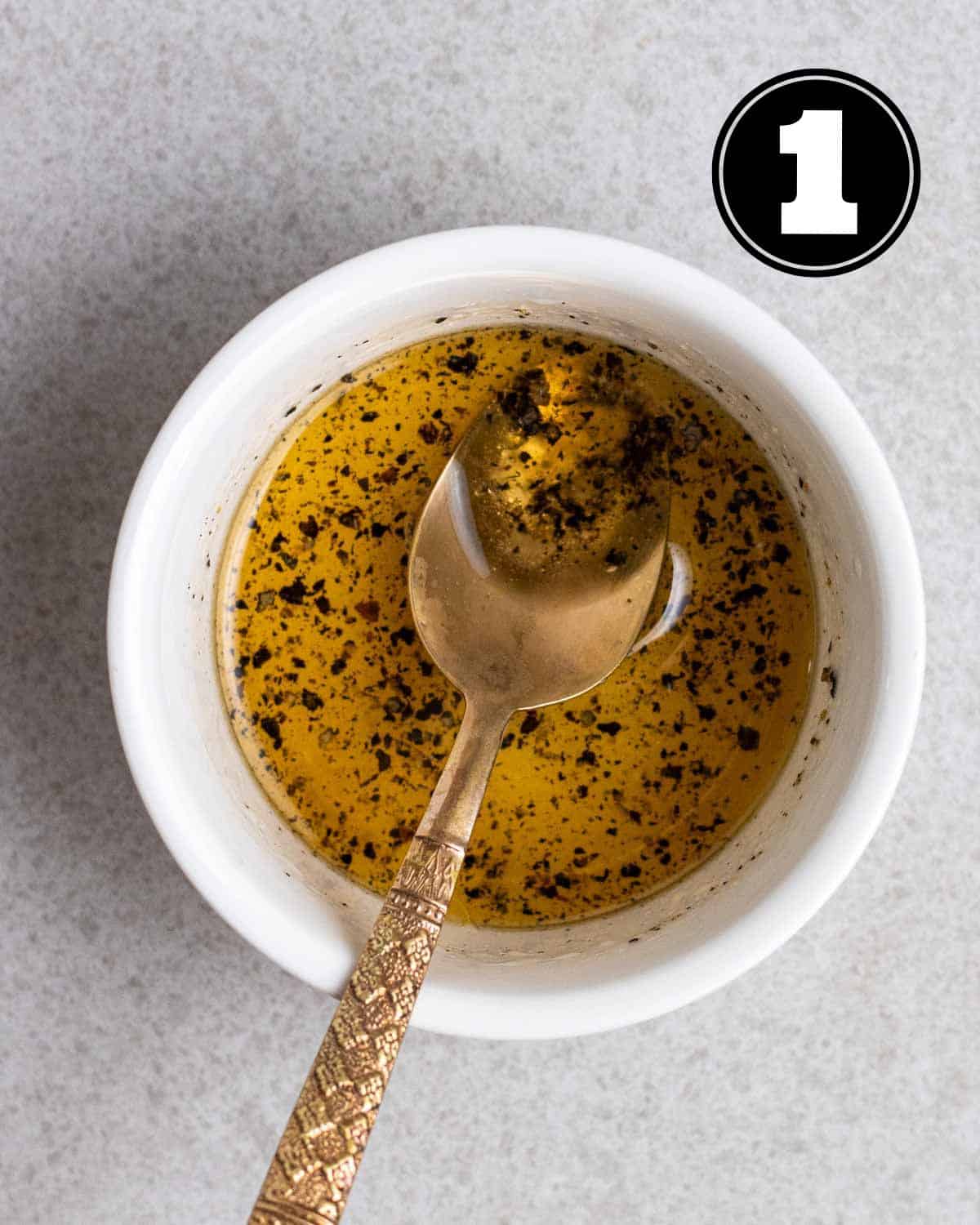 Salad dressing in a ramekin with a teaspoon beside.
