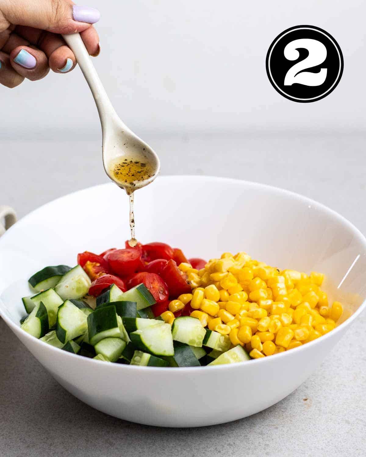 Pouring dressing into a bowl of chopped cucumber, tomatoes, and corn.