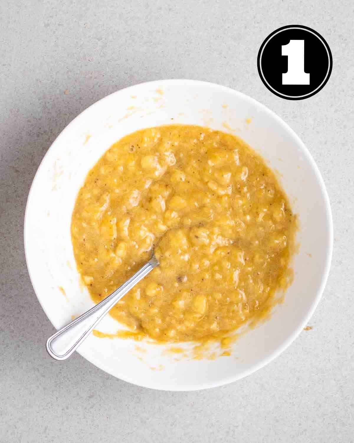 Mashed bananas in a white mixing bowl with a fork beside.