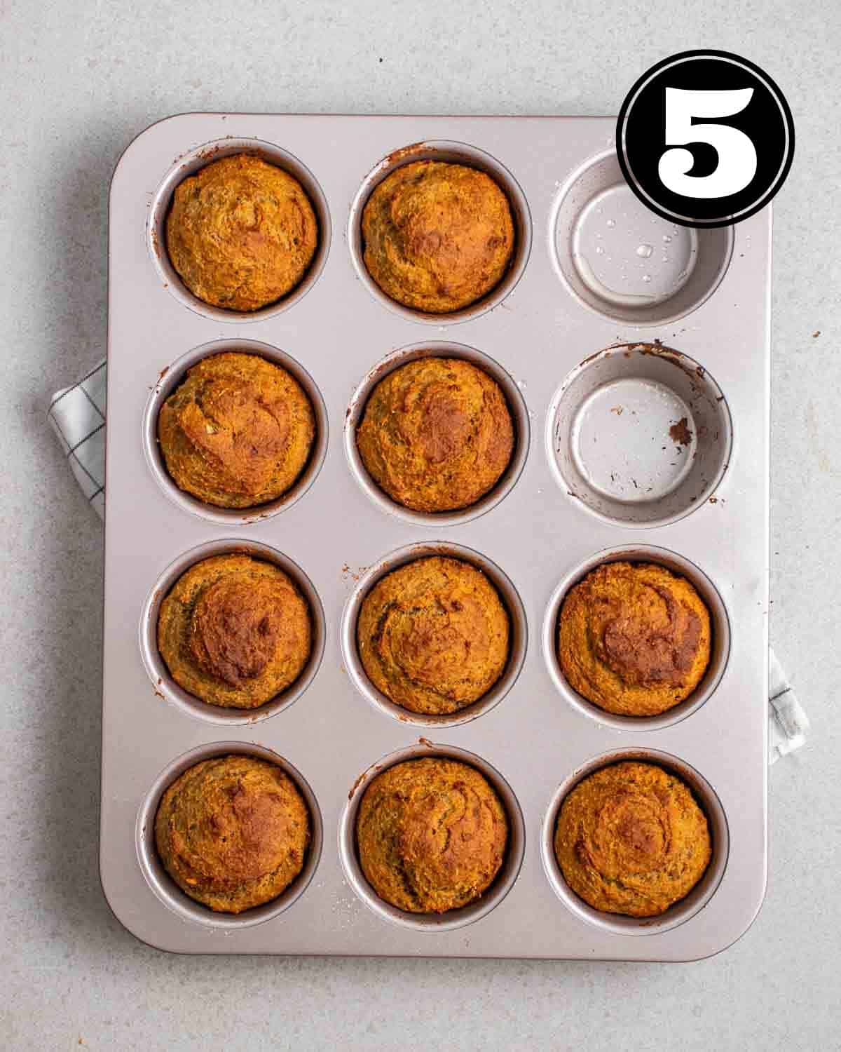 Baked muffins in a tray on a white folded teacloth.