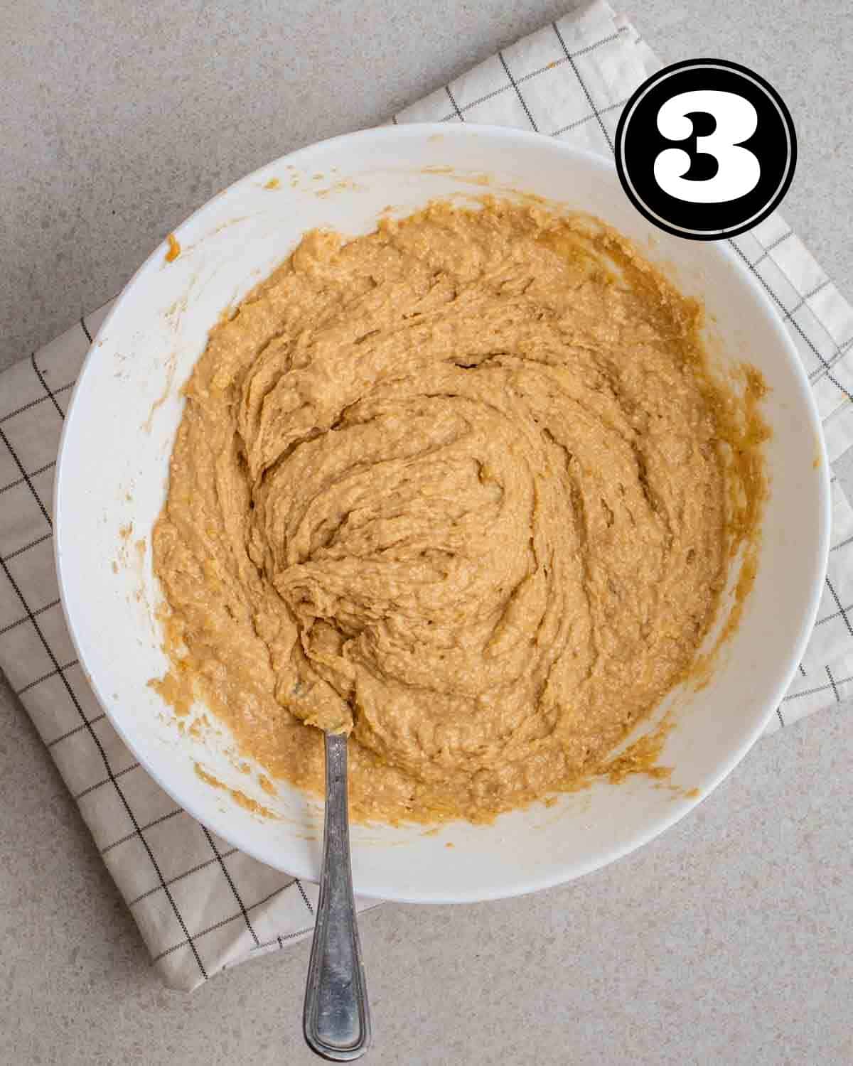 Muffin batter in a white bowl with a fork beside on a white folded teacloth.