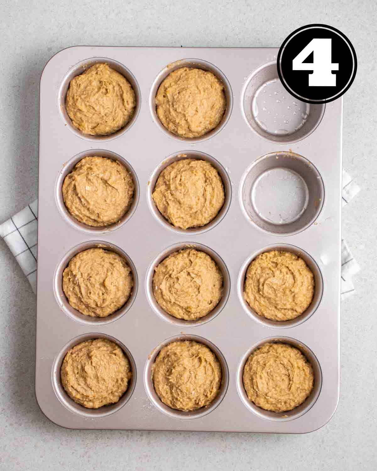 Unbaked muffins in a muffin tray on a white folded teacloth.