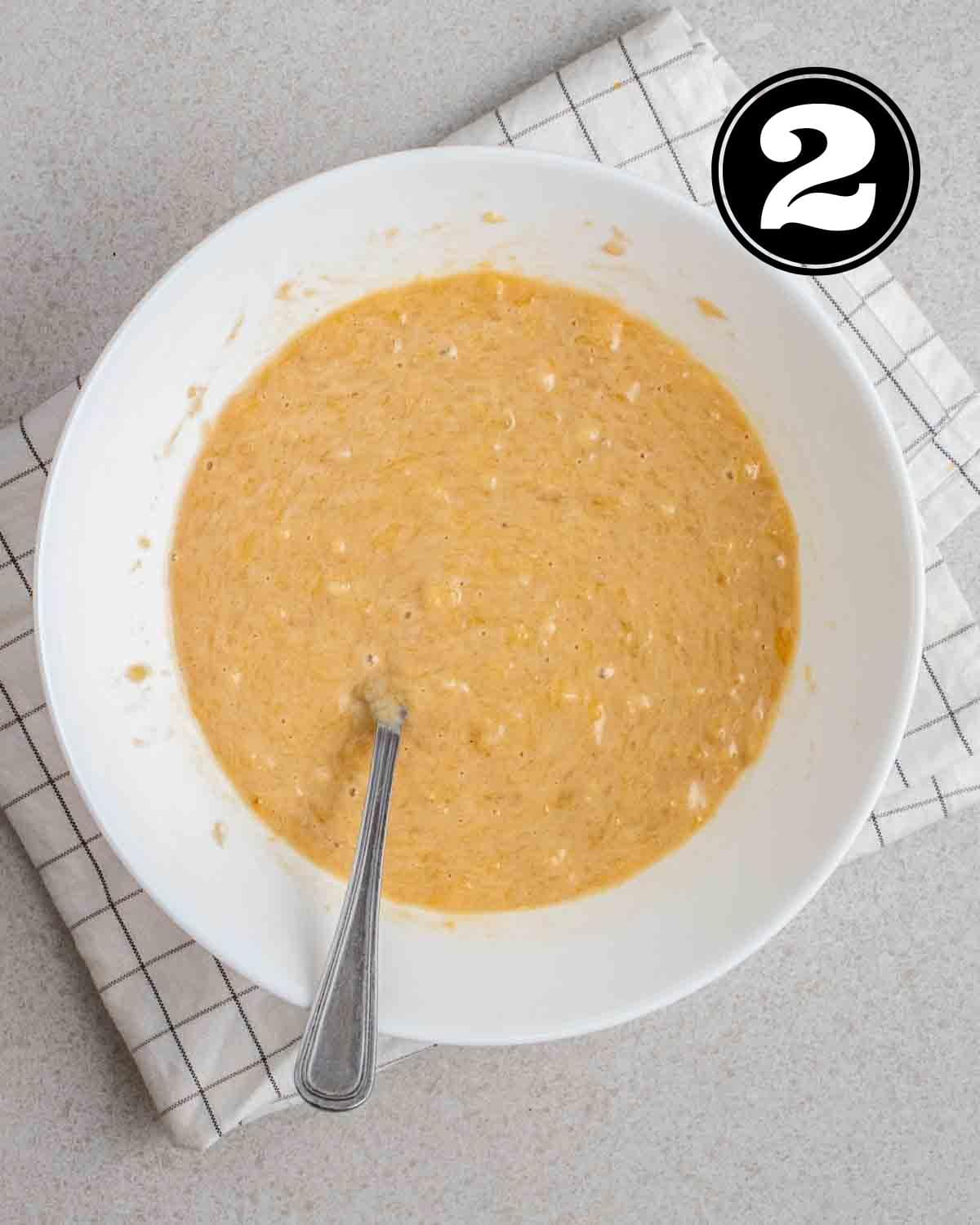 Wet ingredients in a white bowl with a fork beside on a white folded checkered teacloth.