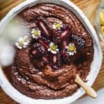 Abowl of chocolate sauce served with a spoon topped with edible flowers.