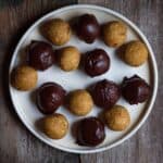 A plate of bliss balls with some of them coated with chocolate.