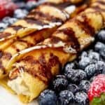 2 rolled up crepes with strawberries and blueberries beside on a white plate.