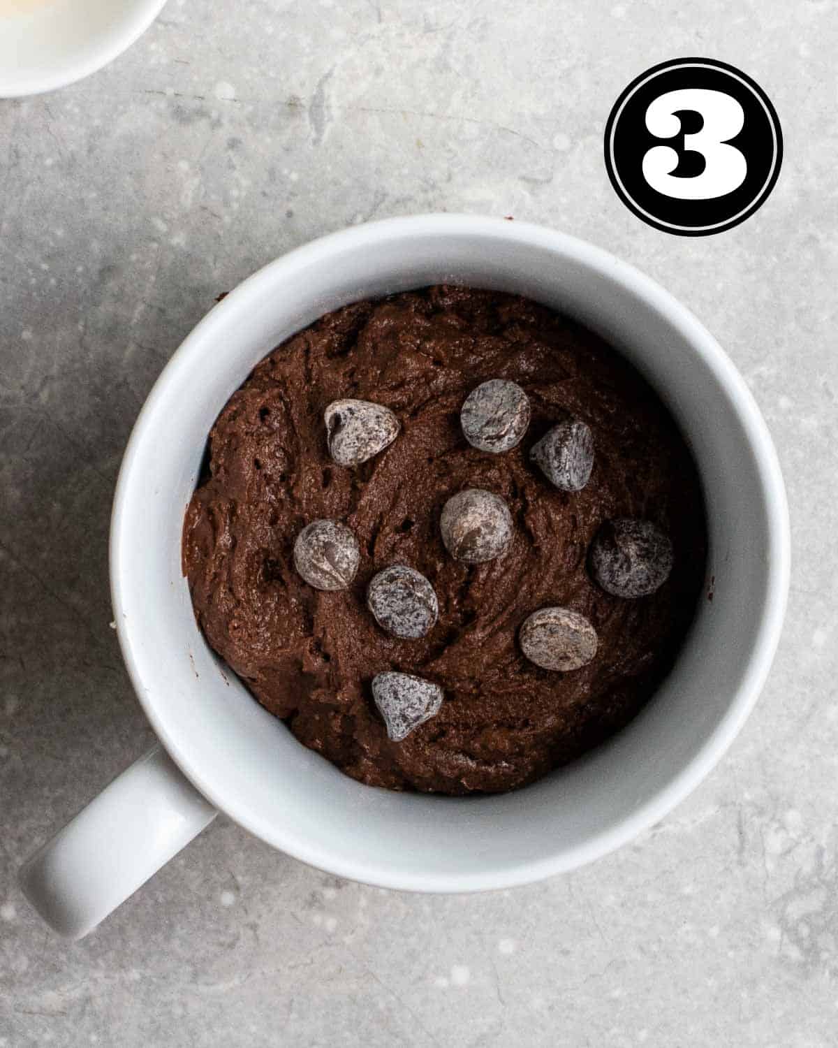Uncooked mug cake in a cup topped with chocolate chips.