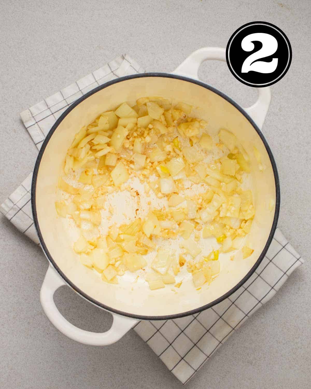 Cooked onion and garlic in a Dutch oven on a white folded checkered teacloth.