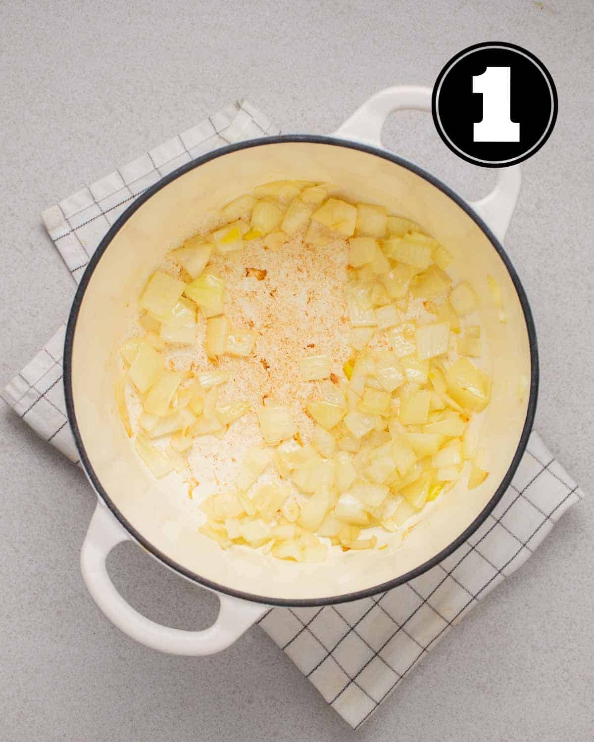 Cooked onion in a Dutch oven on a white folded teacloth.