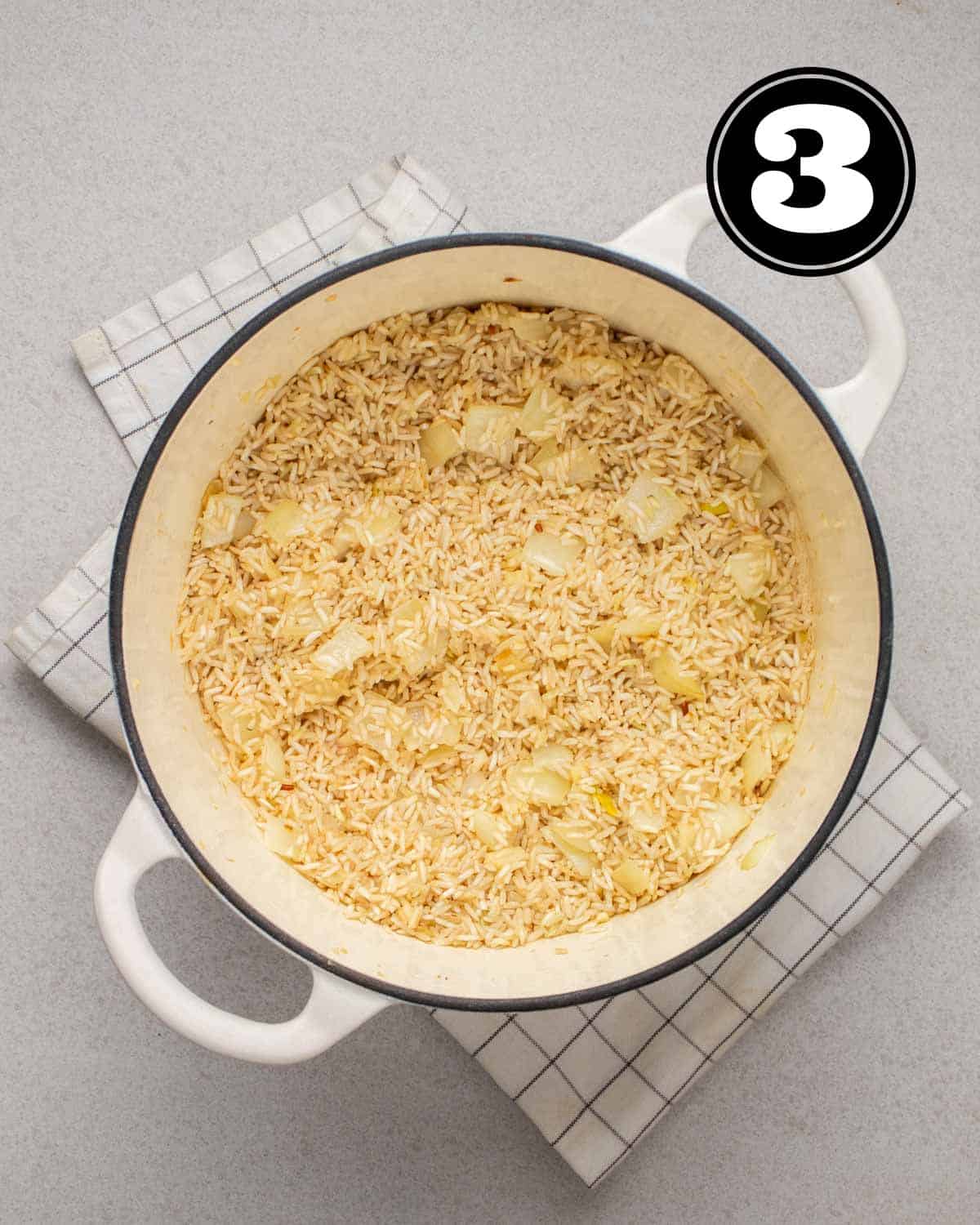 Toasted rice in a white Dutch oven on a white folded teacloth.