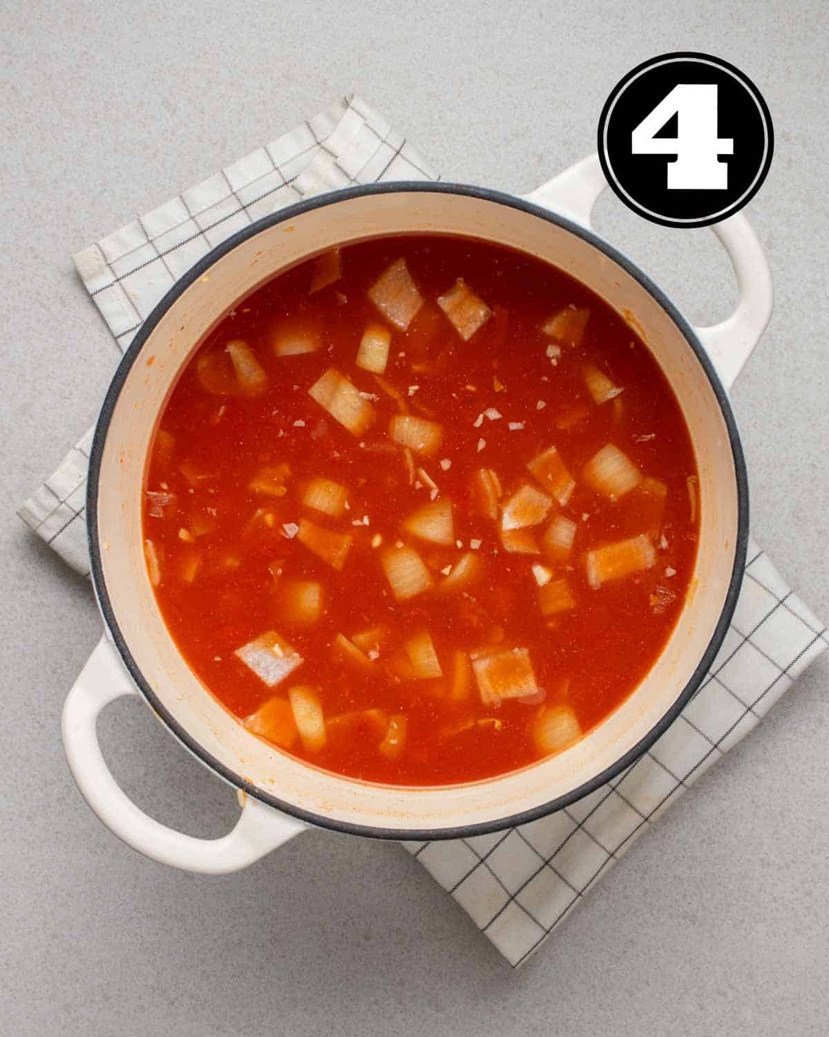 Tomatoes, broth, and rice in a white Dutch oven on a white folded teacloth.