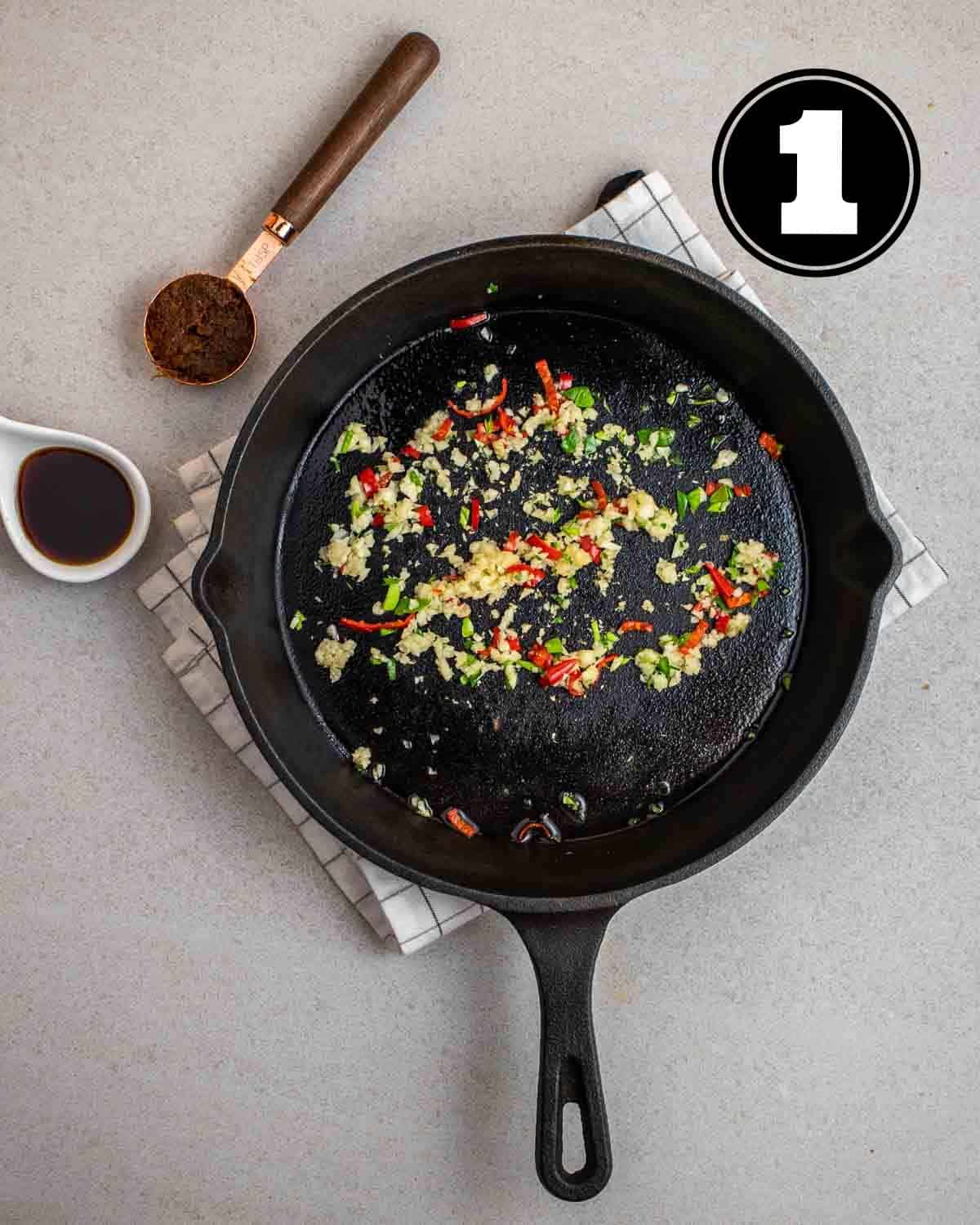 Cooked chiles, garlic, kaffir lime leaves, and tom yum paste in a cast iron skillet.