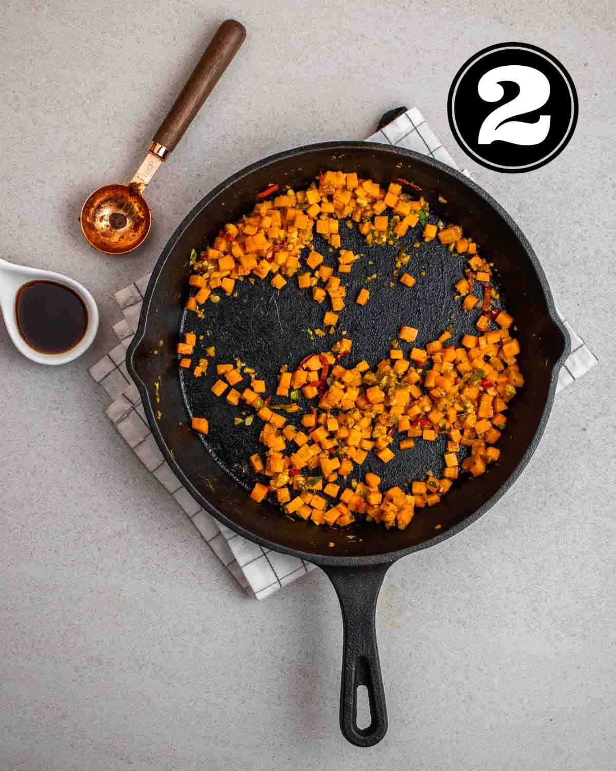 Cooked carrots in a cast iron skillet on a folded white teacloth with a tablespoon and soy sauce beside.
