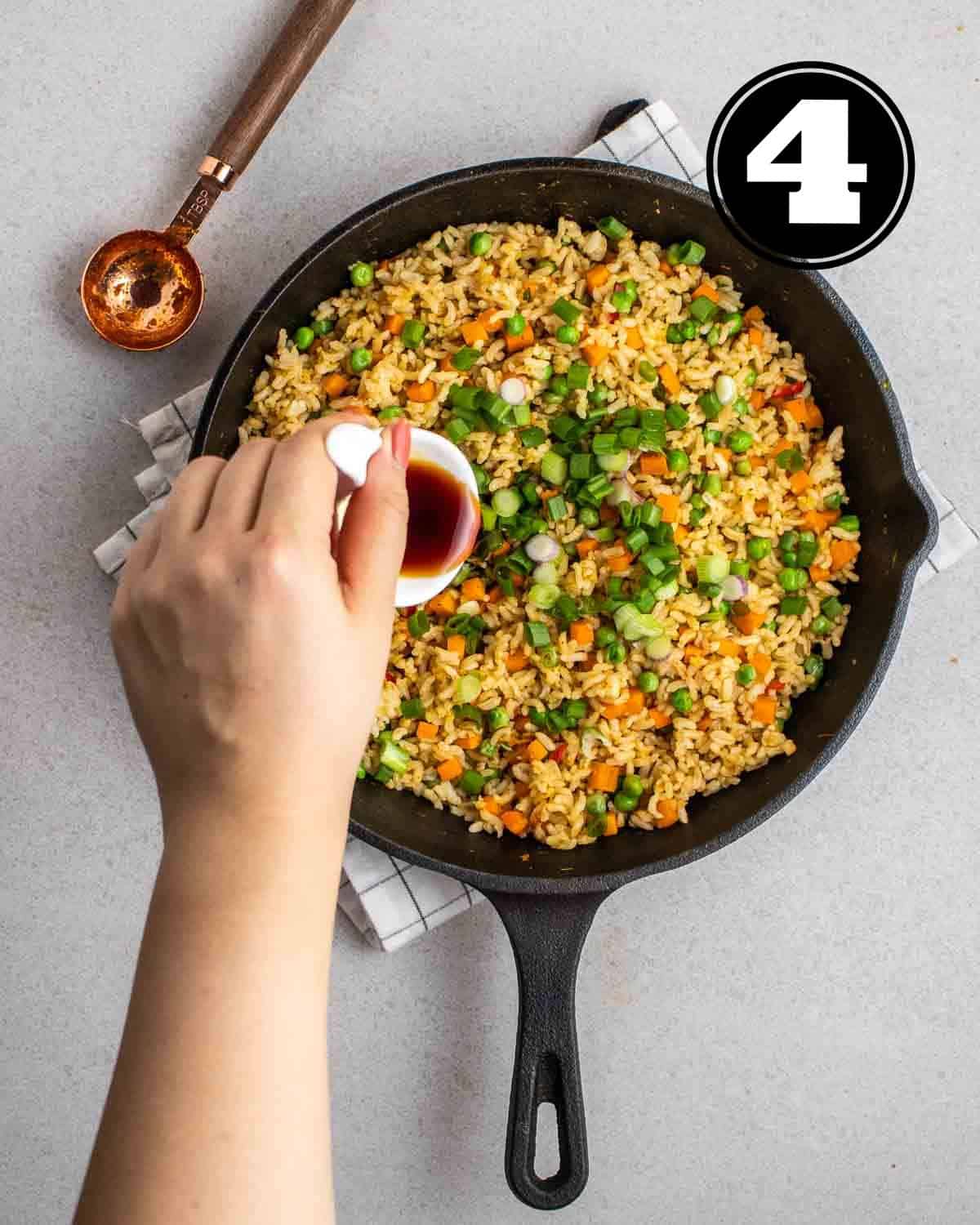 Pouring soy sauce into a pan of tom yum fried rice on a white folded teacloth.