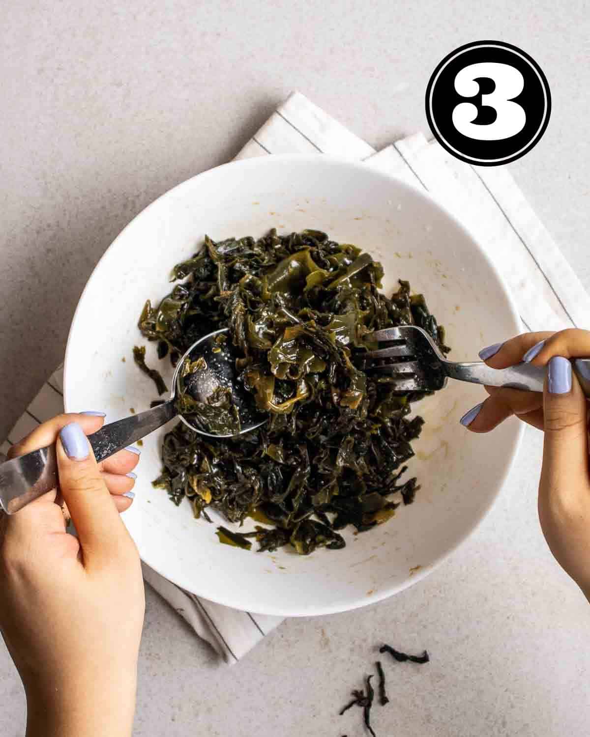 Tossing salad in. bowl on a white folded teacloth.
