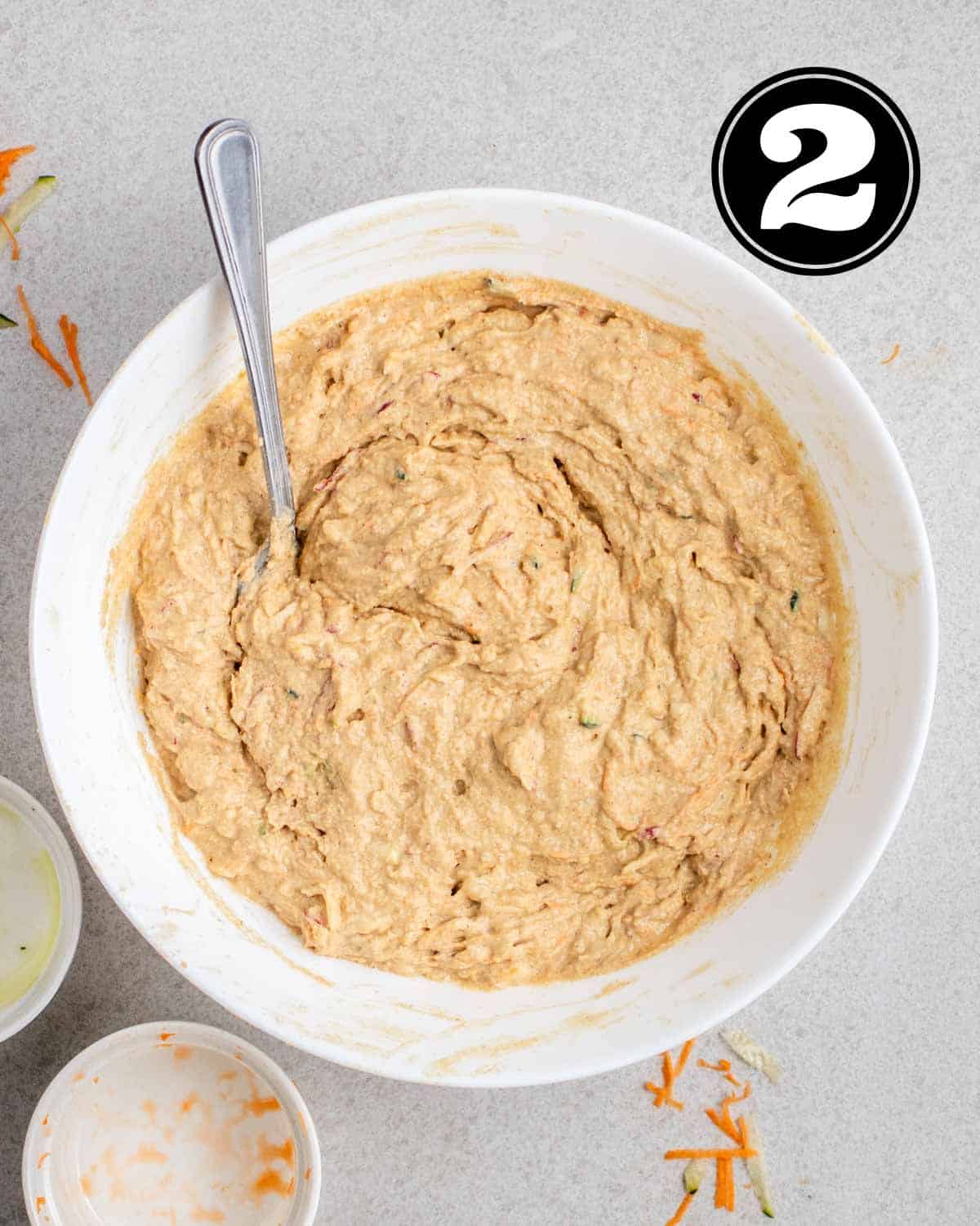 Muffin batter in a bowl with a spoon with 2 empty ramekins beside.