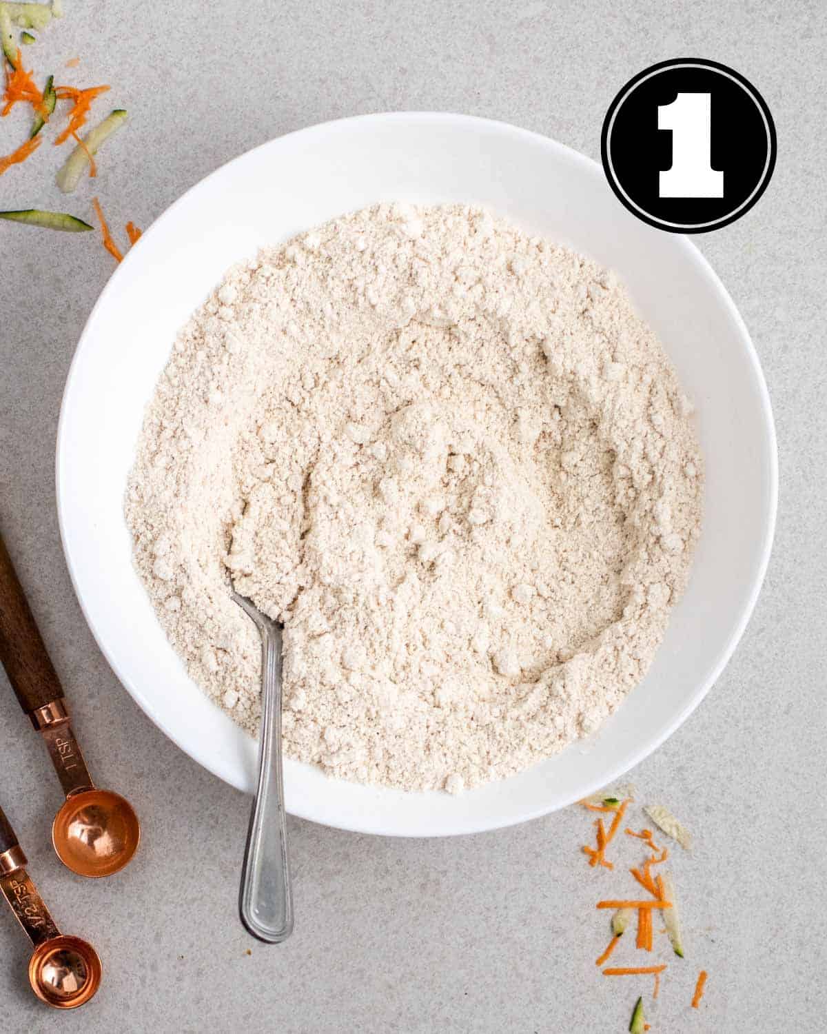 Dry ingredients for muffins in a bowl with 2 measuring spoons beside.