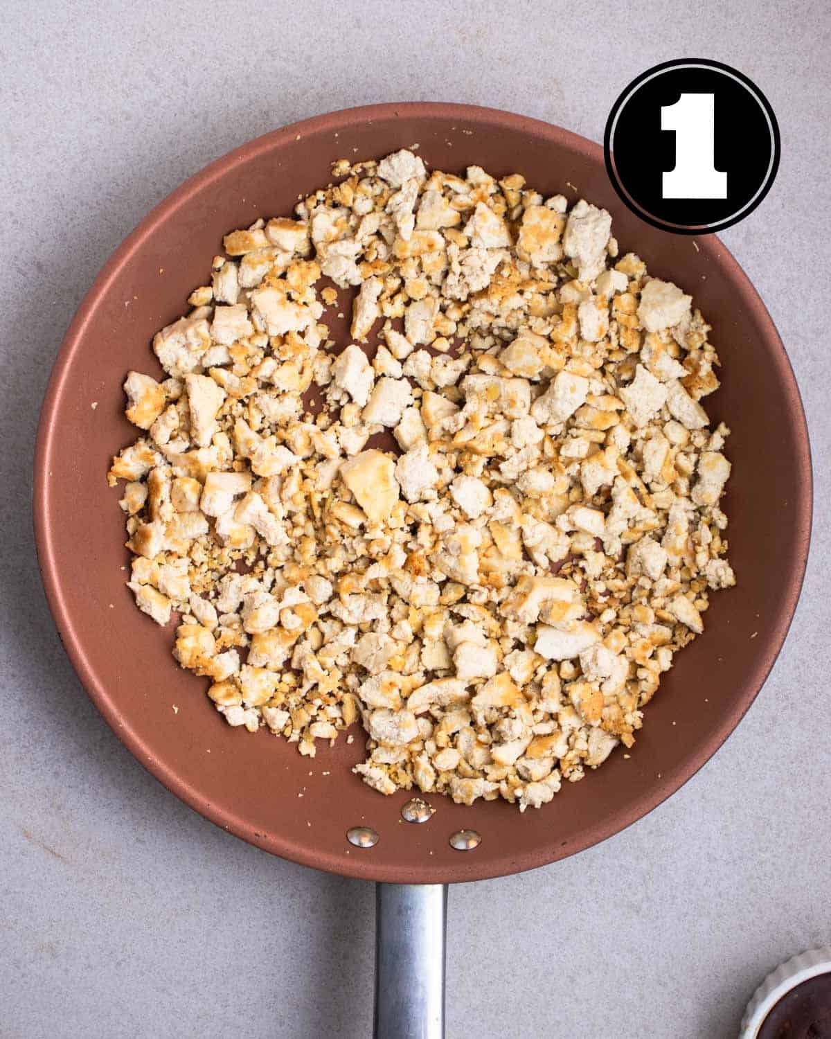 Crumbled, cooked tofu in a pink non-stick pan.
