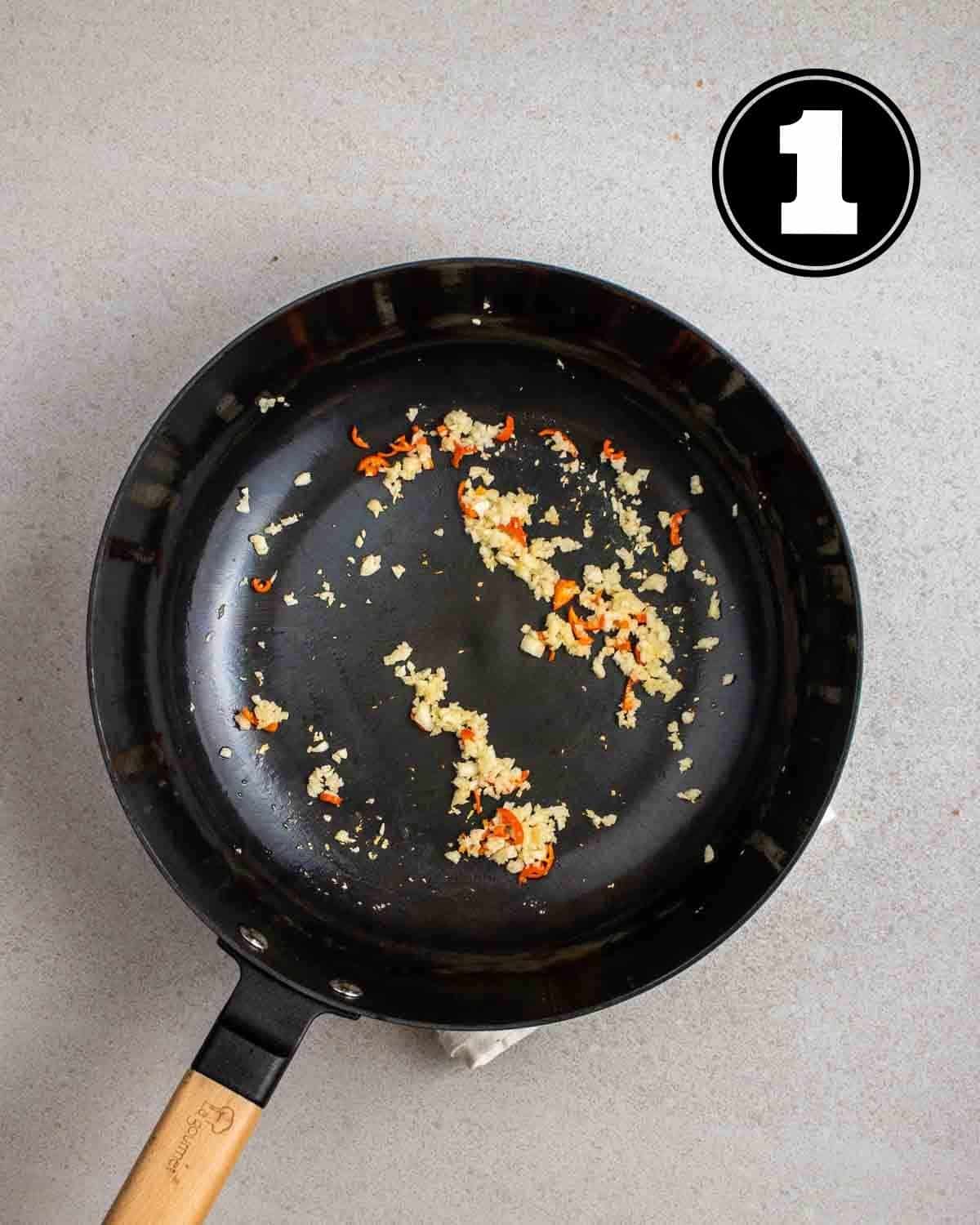 Cooked garlic and chilies in a wok on a white folded teacloth.