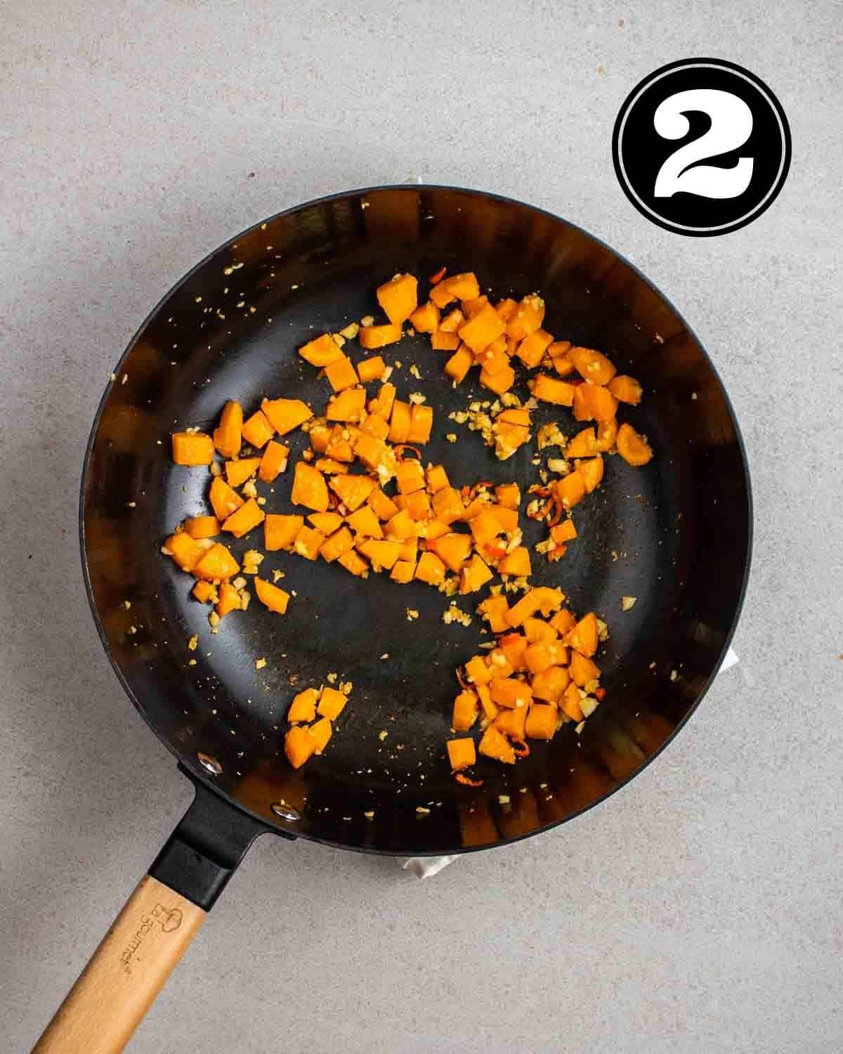 Cooked diced carrot and aromatics in a wok.
