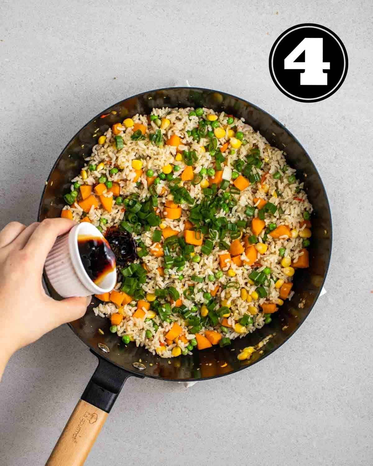 Pouring sauce into a wok of cooked vegetables and rice.