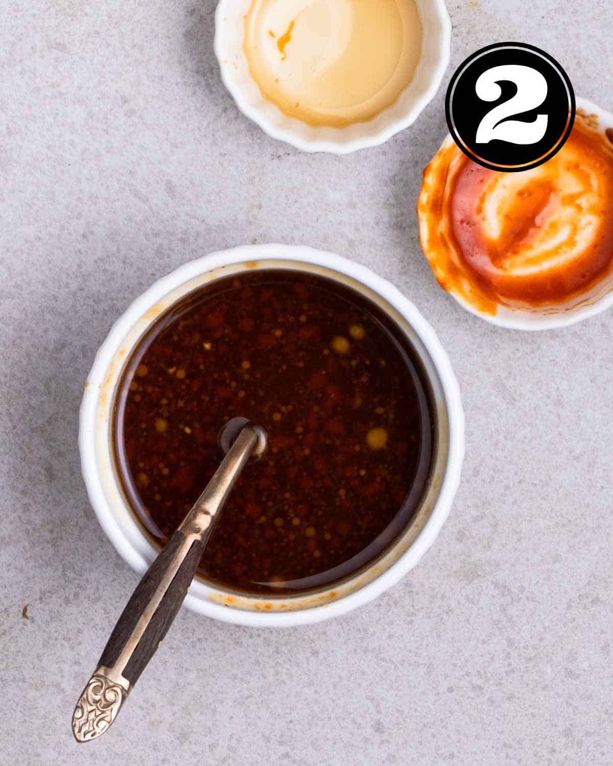 Stir-fry sauce in a white ramekin with a teaspoon beside and 2 empty sauce dishes in the background.