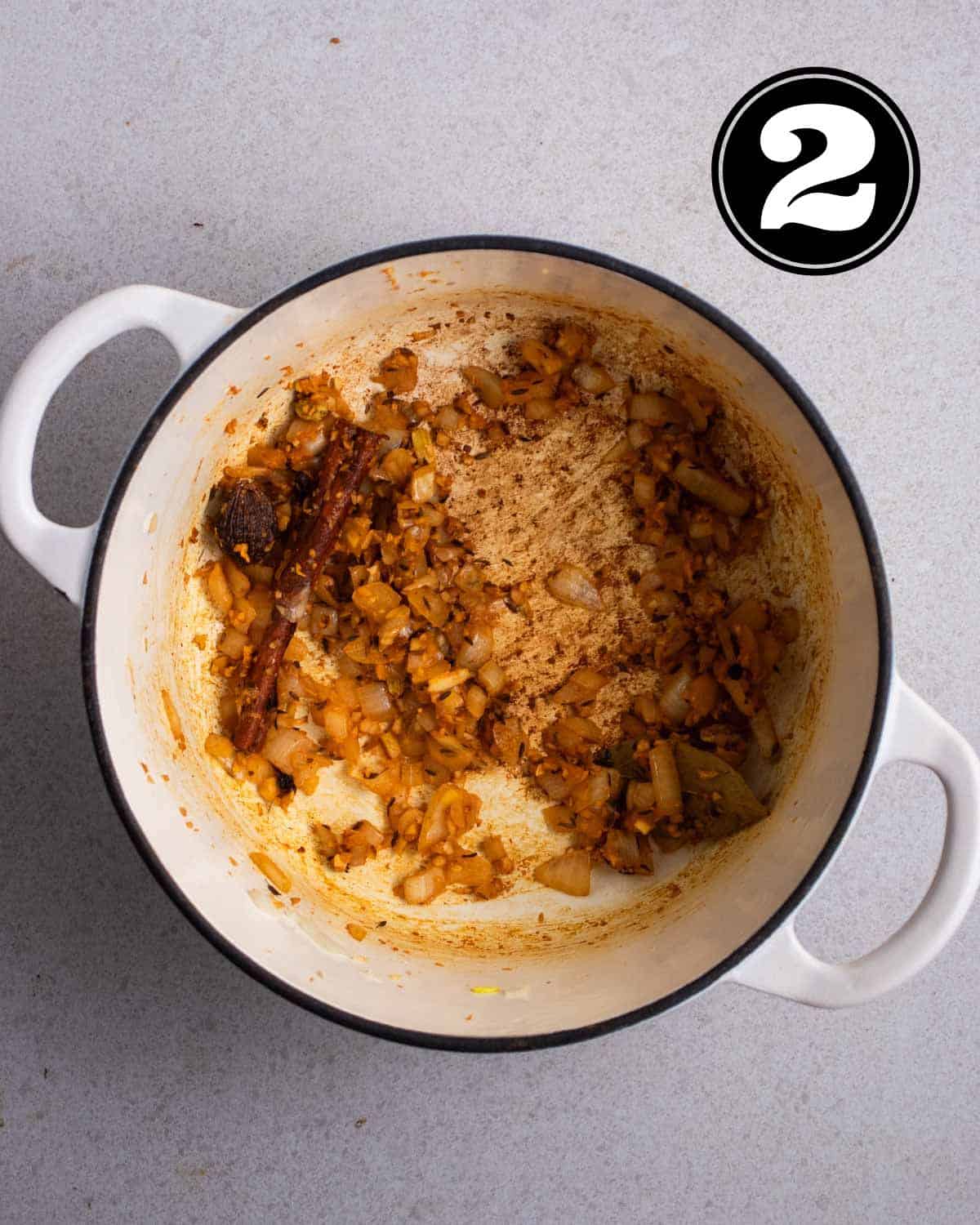 Cooked aromatics and spices in a white Dutch oven.